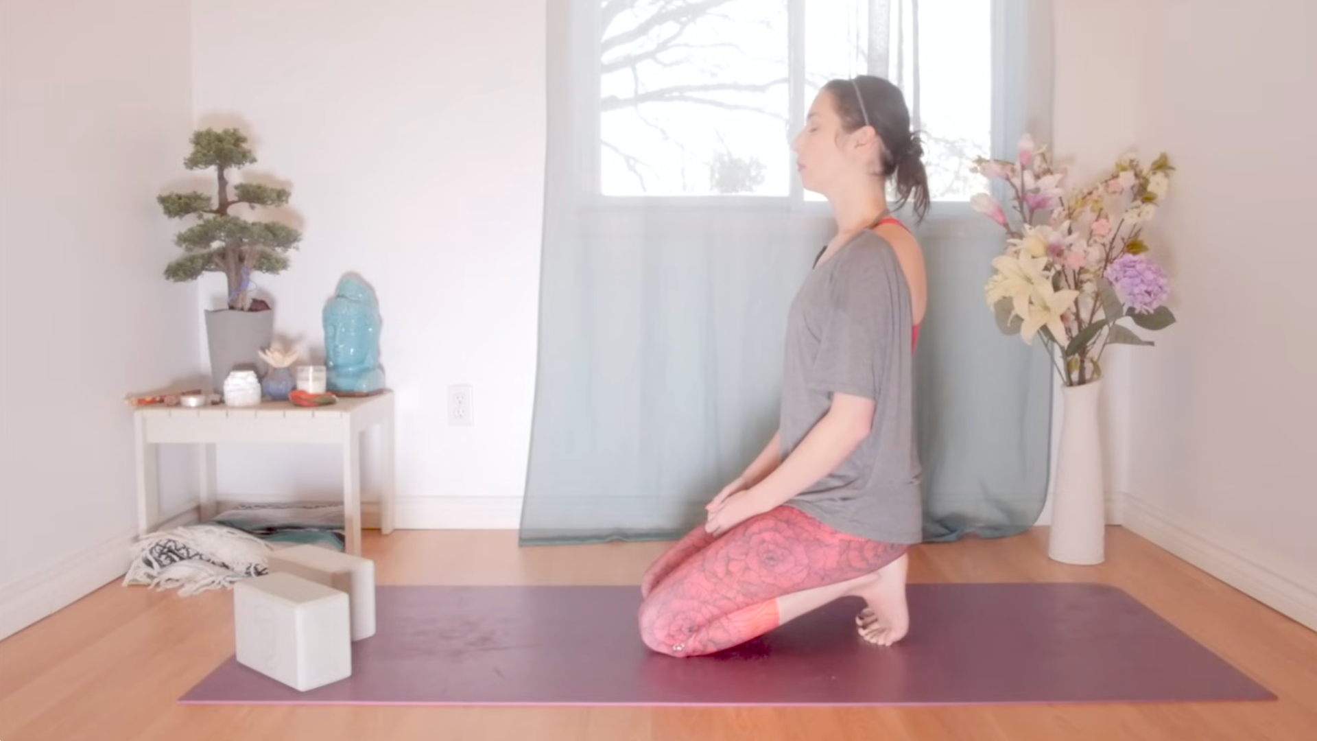 Woman kneeling on a yoga mat with her toes tucked under while practicing yin yoga for root chakra balancing