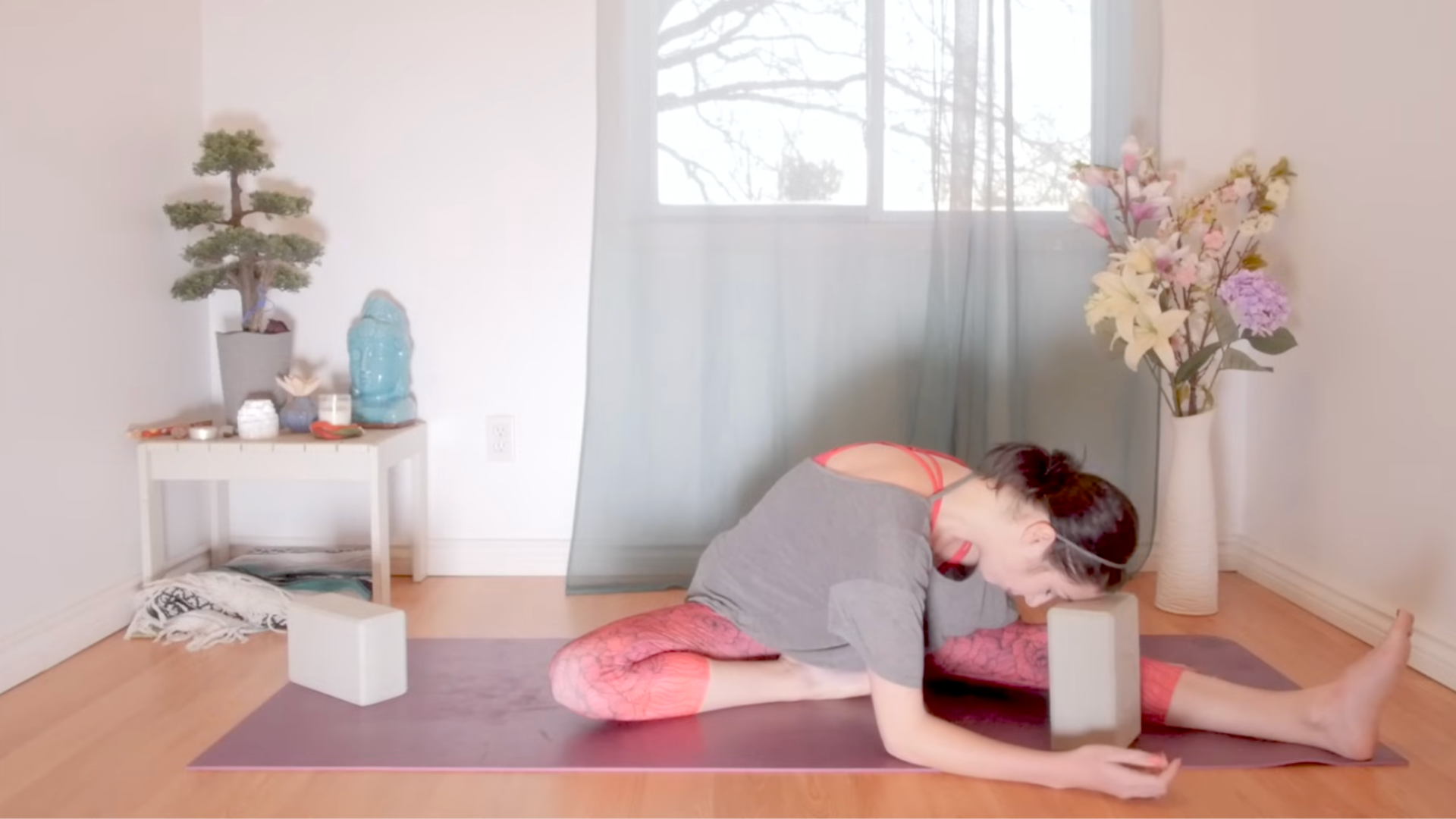 Woman sitting on a yoga mat with one leg straight and the other bent as she leans forward in the yin yoga pose known as Half Butterfly