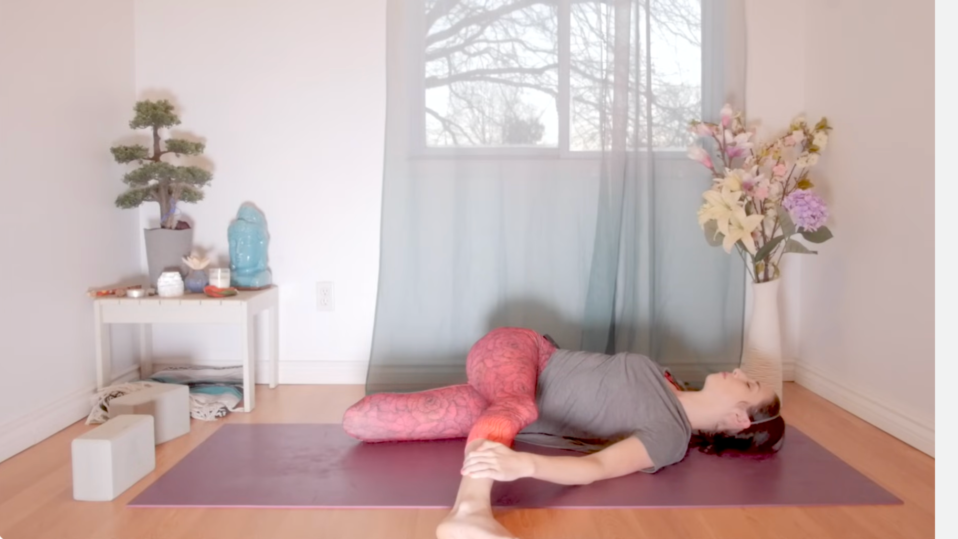 Teacher lying on her back practicing yoga for root chakra balancing in Cat Pulling Its Tail Pose
