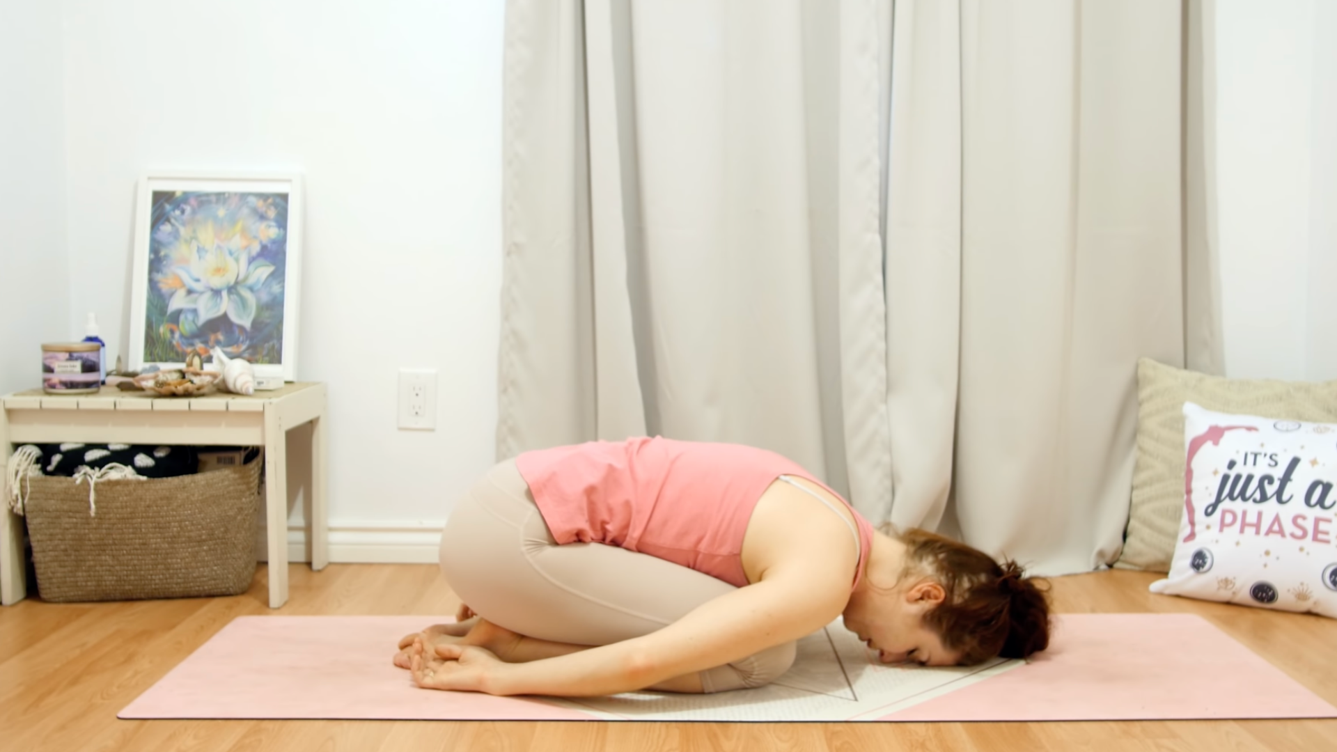 Yoga teacher on a mat in a version of Childs Pose with her arms alongside her body