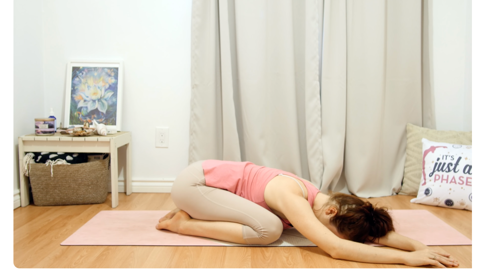 Woman lying on a mat in Child's Pose while taking a side stretch with her arms off to one side