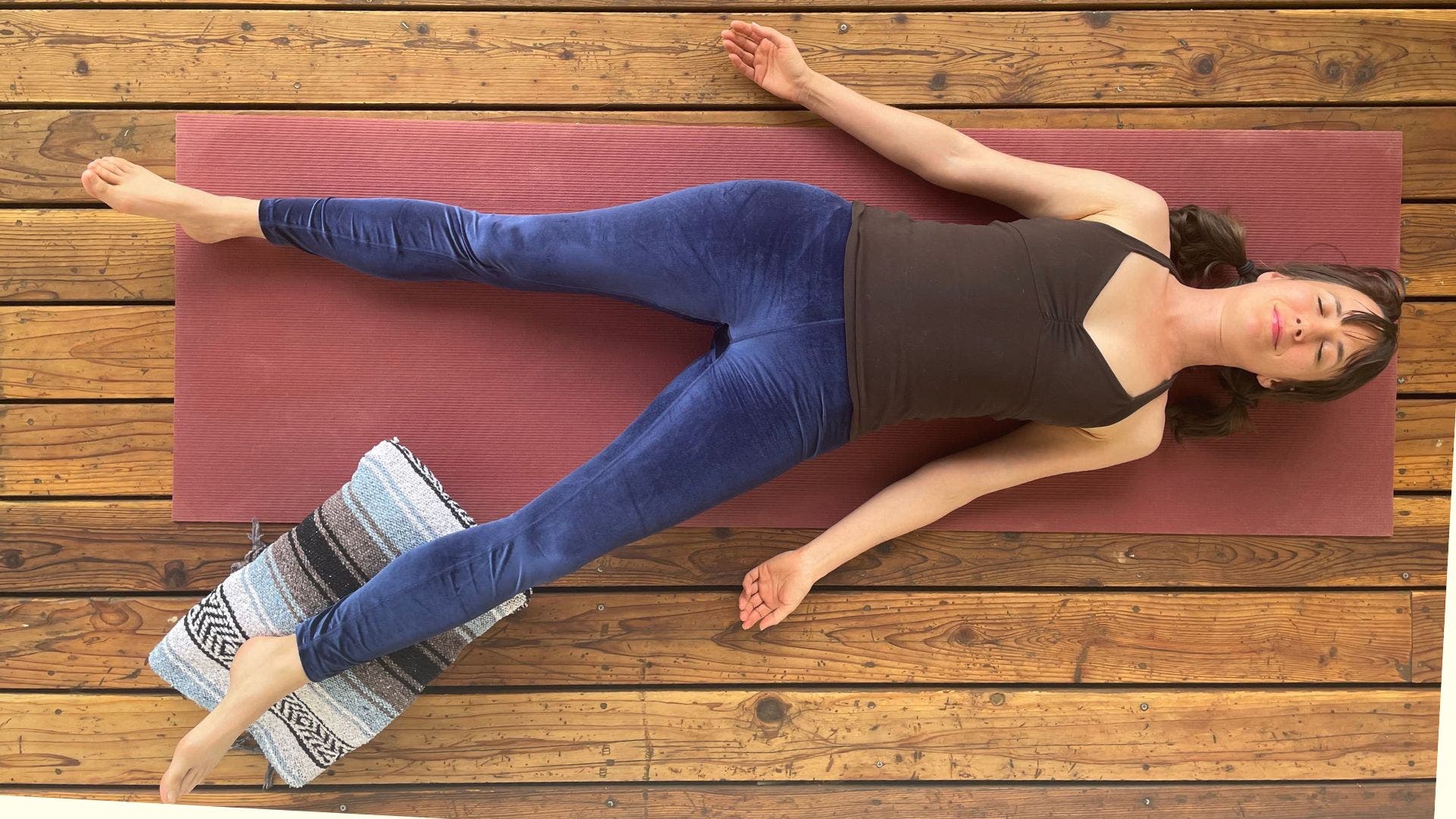 Image of yoga teacher Amber Burke practicing asymmetrical Savasana, with one folded blanket underneath her left calf.