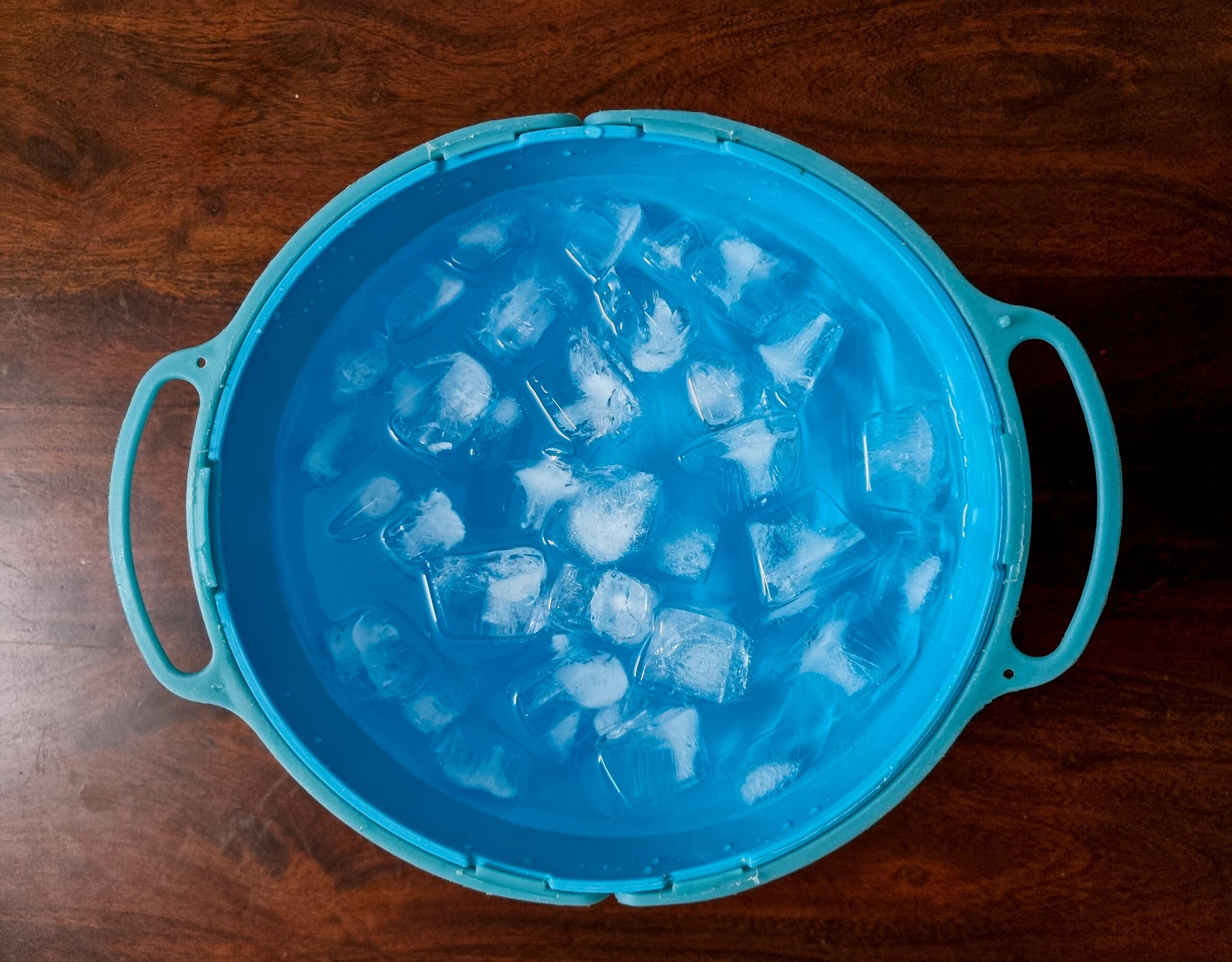 Aerial shot of blue bowl of ice water on a brown wooden table.