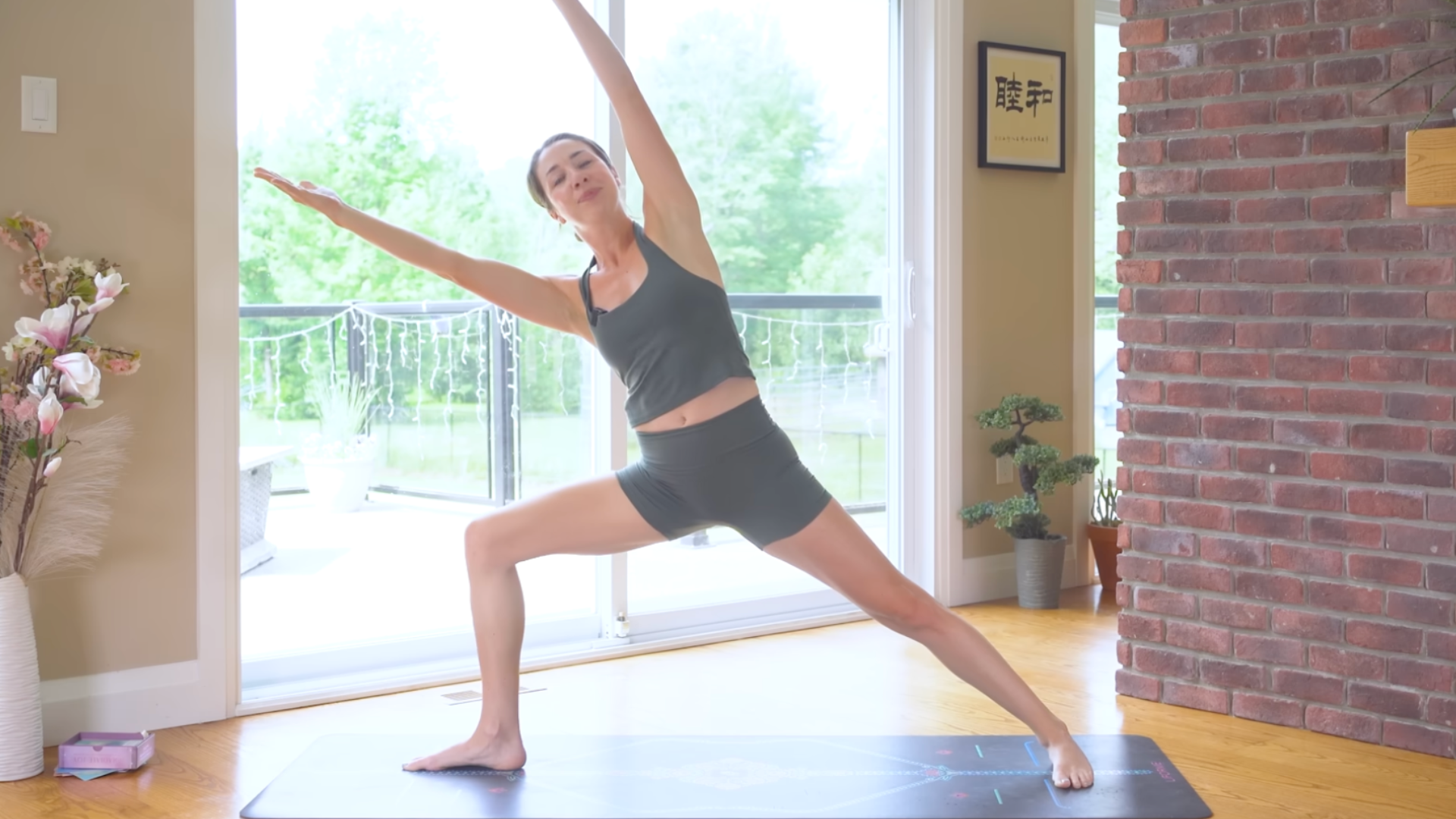 Woman on a yoga mat in Warrior 2 with her arms lifted overhead during a 10-minute morning yoga and pilates routine