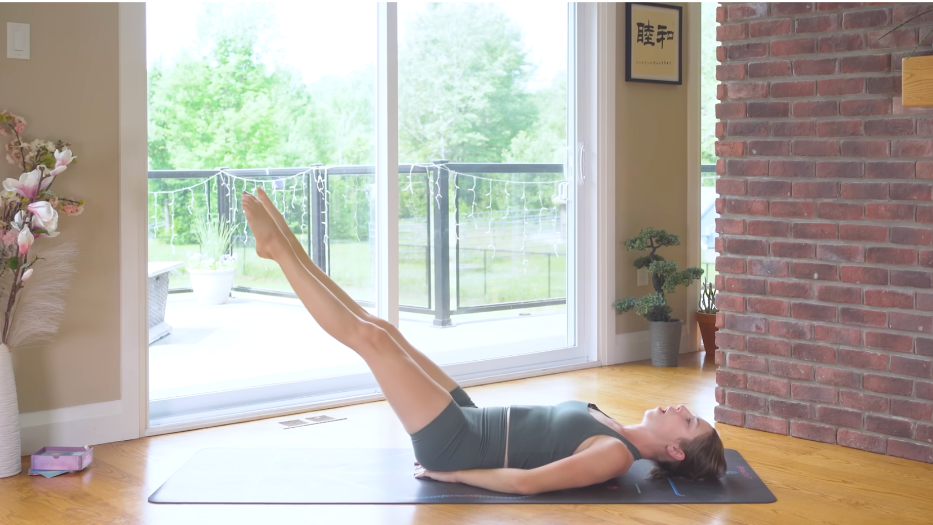 Woman lying on her back with both legs lifted toward the sky but lowered partway toward the mat