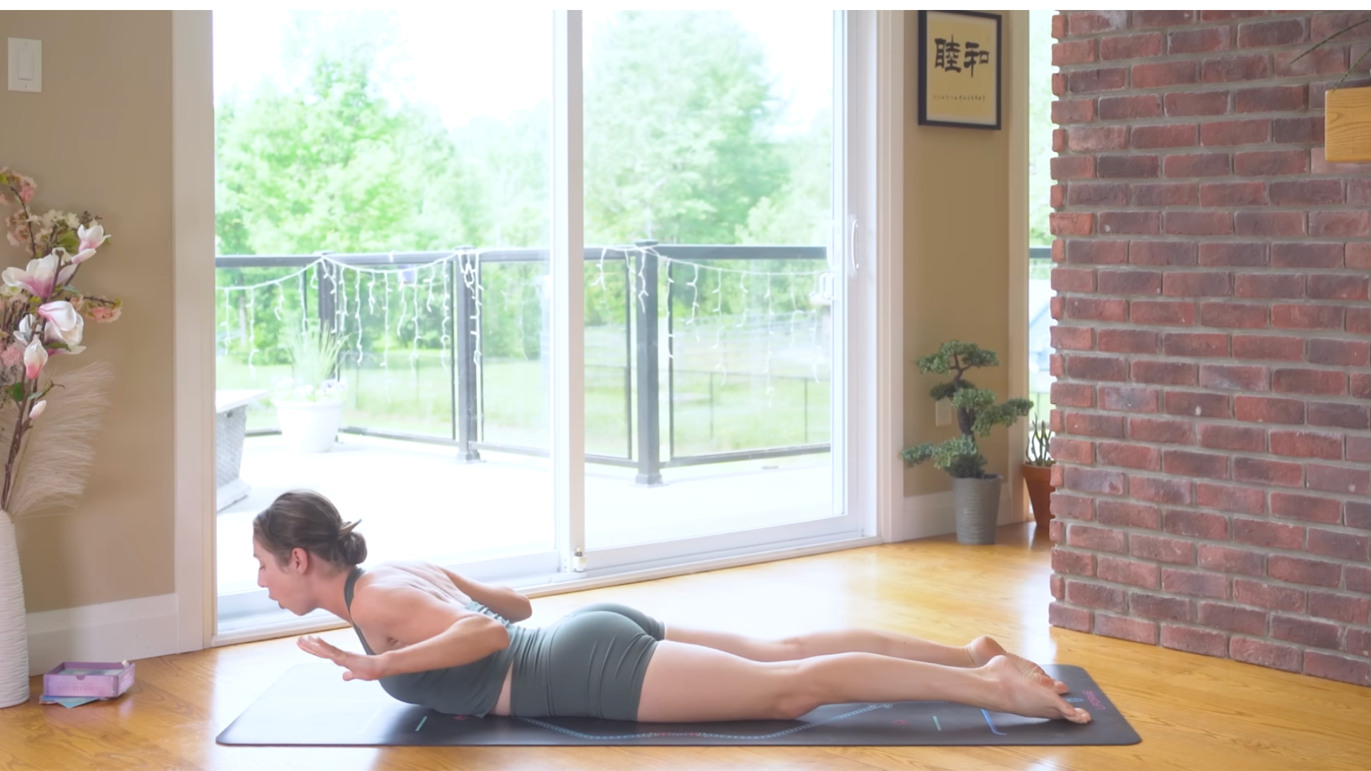 Woman lying on her belly on a yoga mat during a 10-minute morning yoga routine and lifting her chest and palms off the mat in Baby Cobra