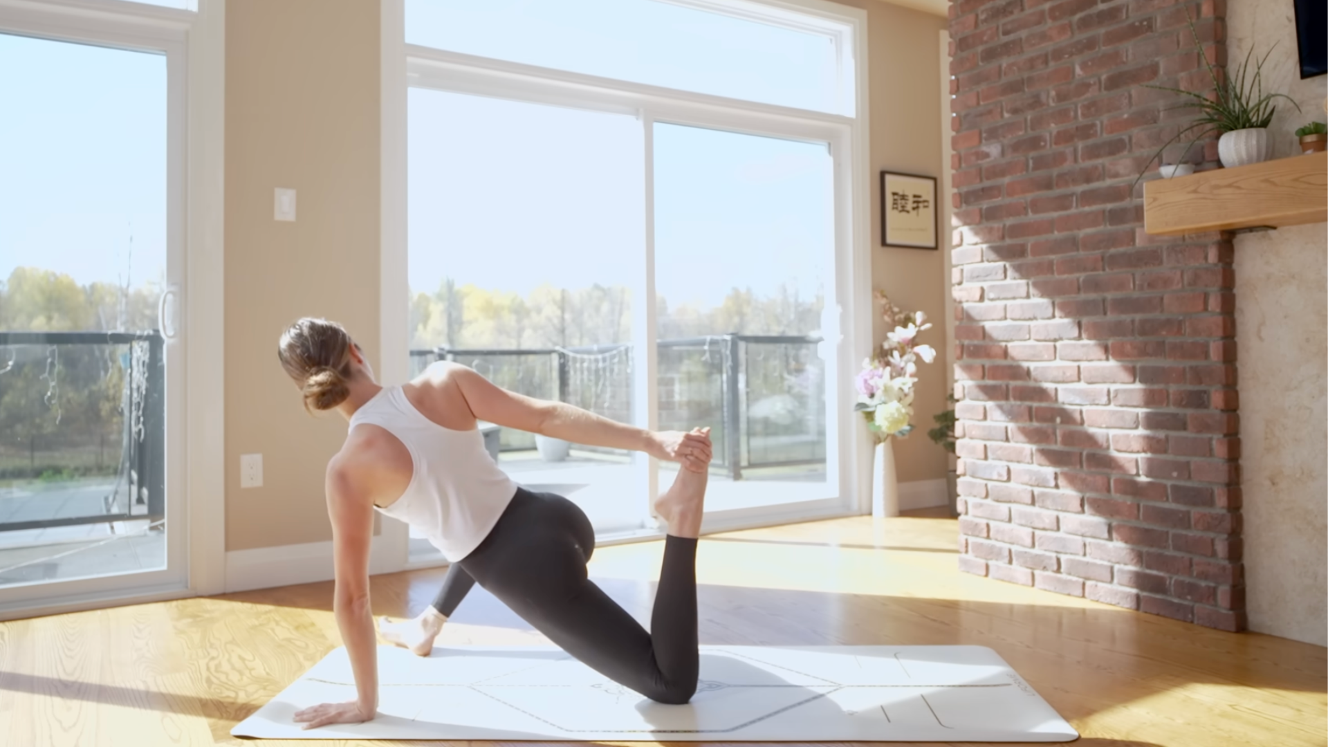 Yoga teacher kneeling on a mat in a Twisted Monkey version of Lizard Pose by grabbing her left foot behind her
