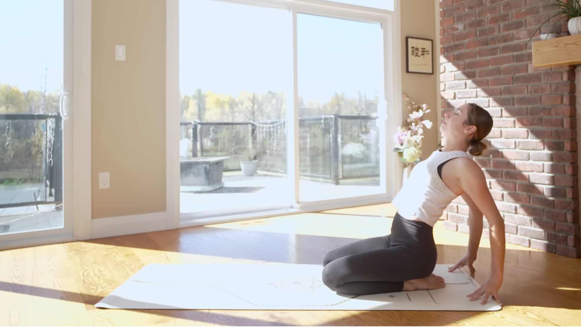 Woman on a yoga mat kneeling with her hands behind her and leaning back into a slight backbend