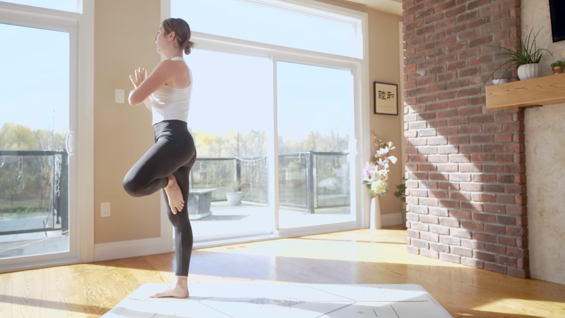 Yoga teacher standing on a mat with her left foot against her inner right thigh in Tree Pose
