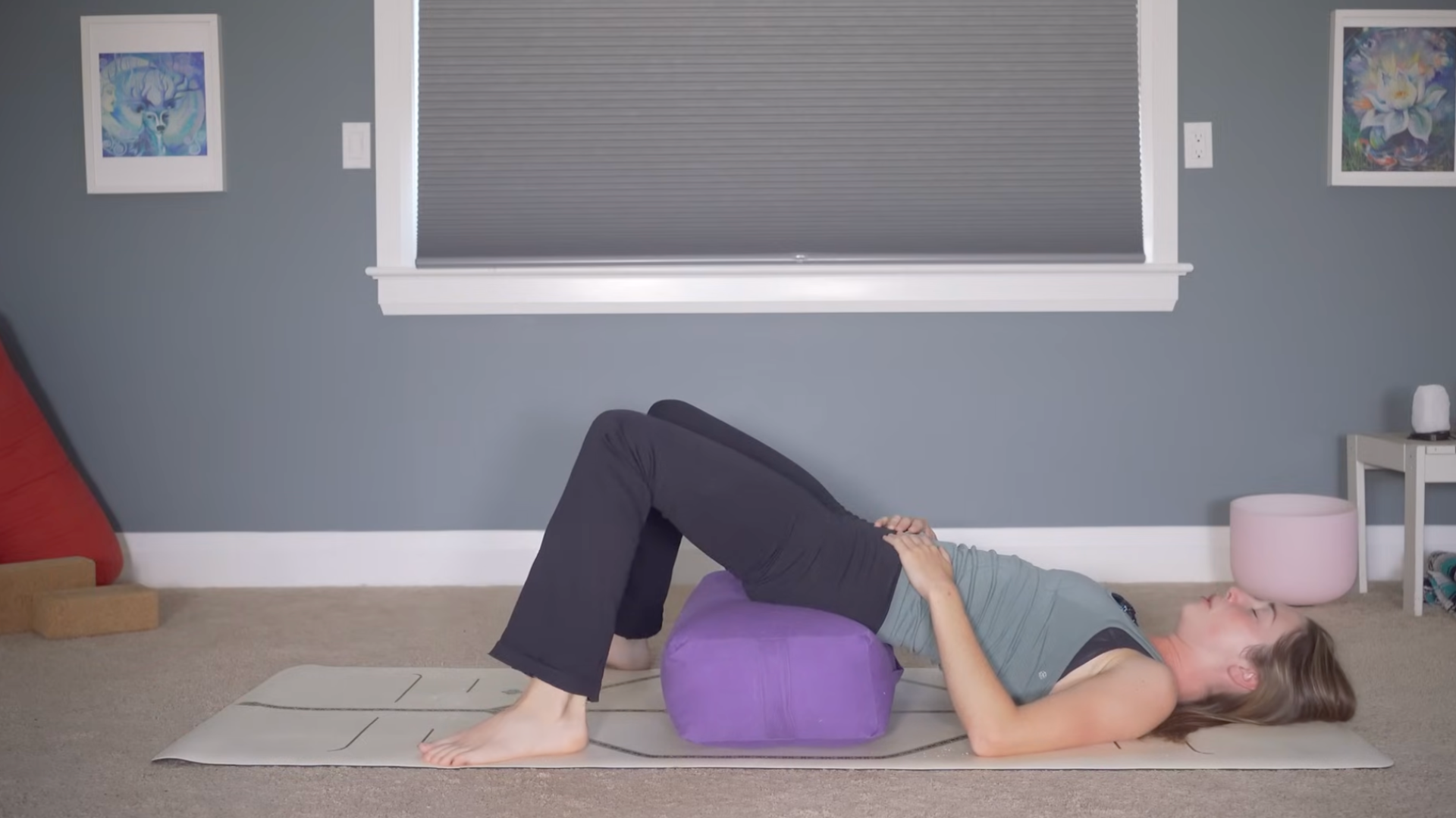 Woman lying on her back with a bolster or prop beneath her low back in bedtime yoga