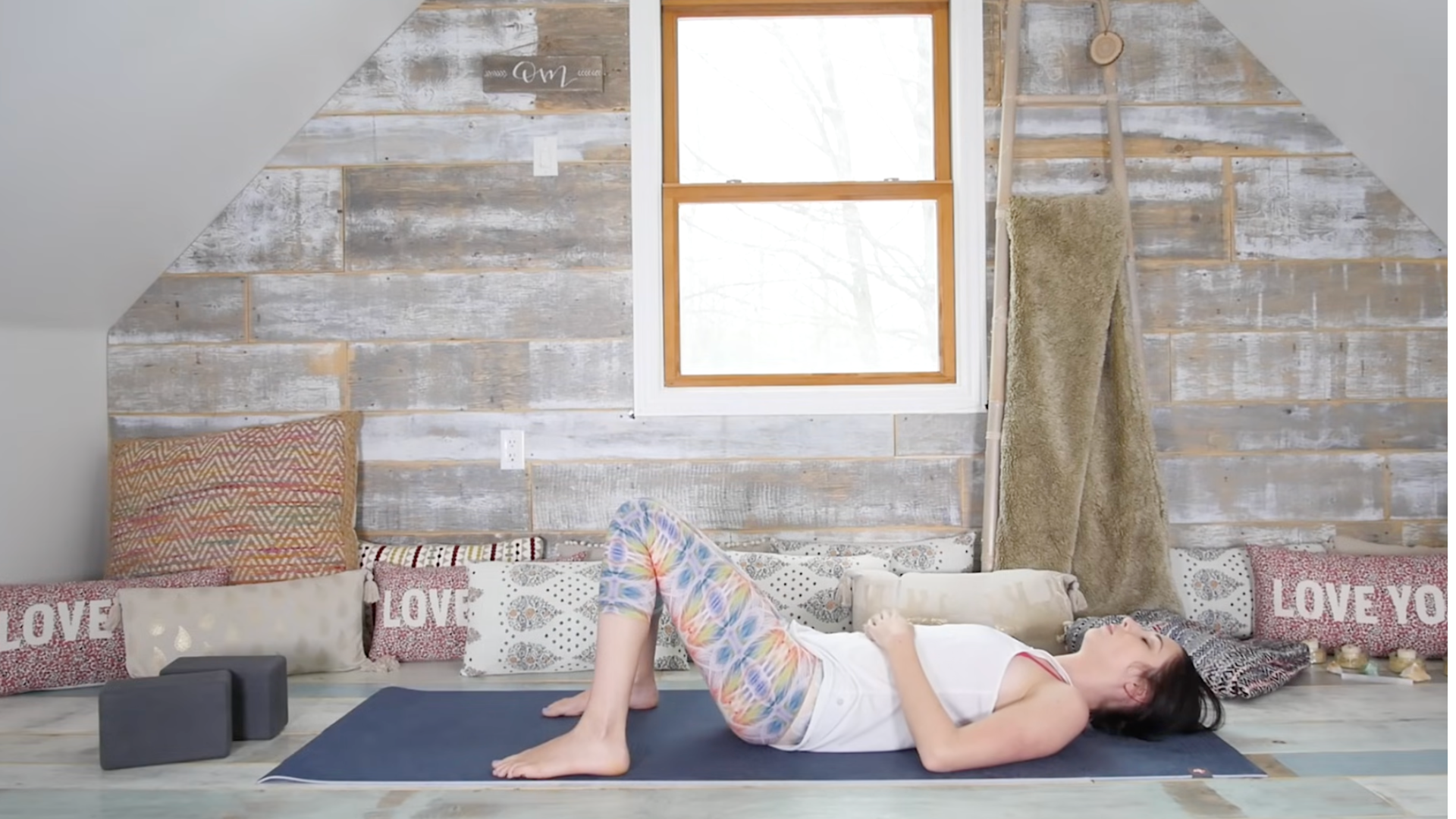 Woman lying on a yoga mat with her knees bent and her feet on the mat with her hands resting on her belly