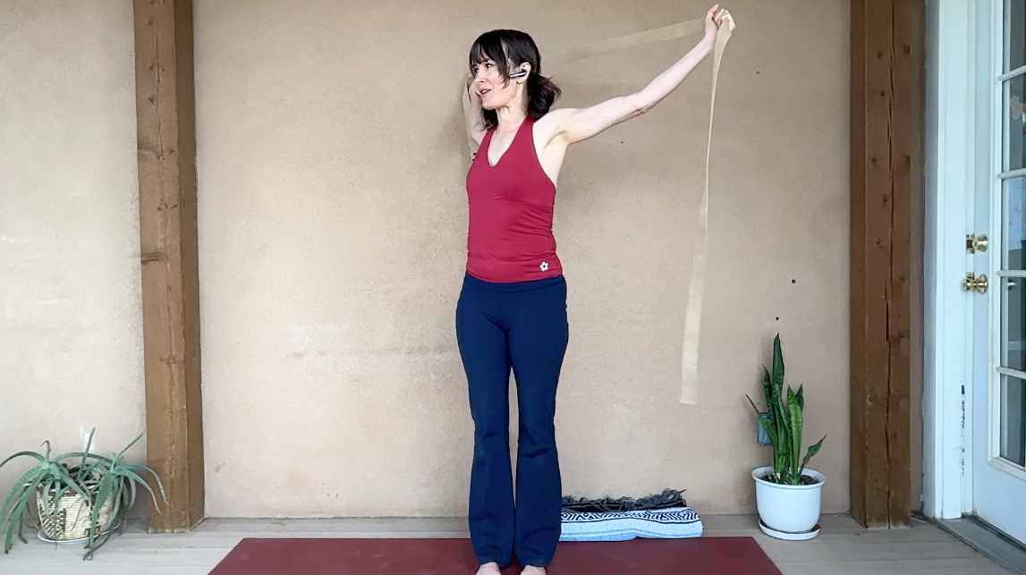 Woman standing on yoga mat holding strap above her head.