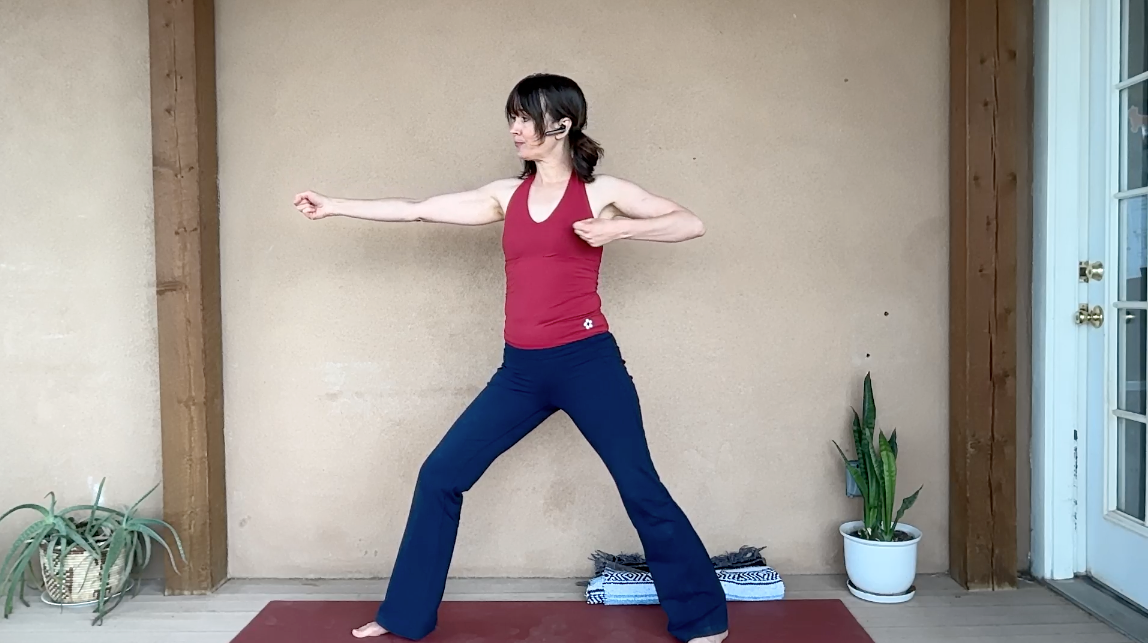 Image of woman standing in Warrior 2 with bow and arrow arms.