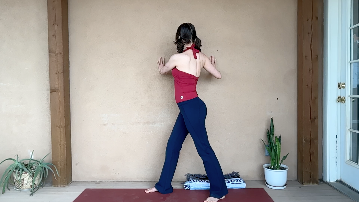 Image of woman standing in Warrior 2 twist against wall.