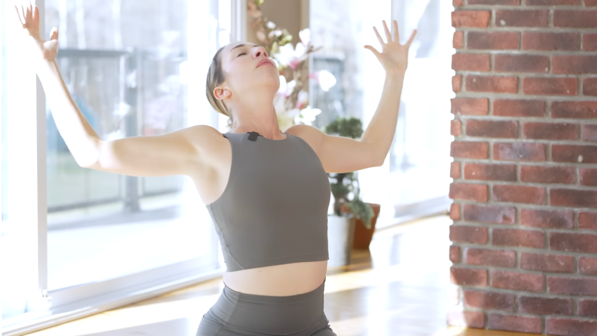 Woman kneeling on a yoga mat with arms outstretched and elbows bent while taking a backbend