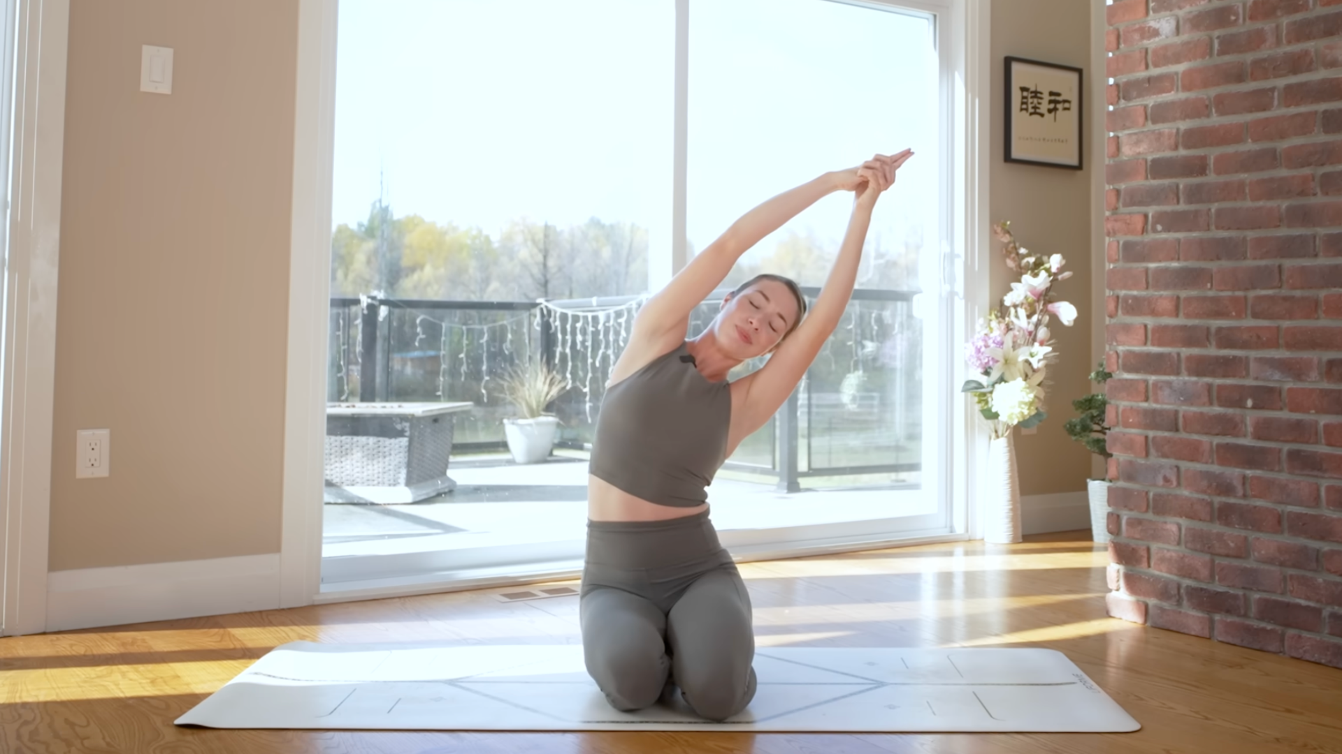 Woman kneeling on a yoga mat with her arms reaching overhead as she leans to one side