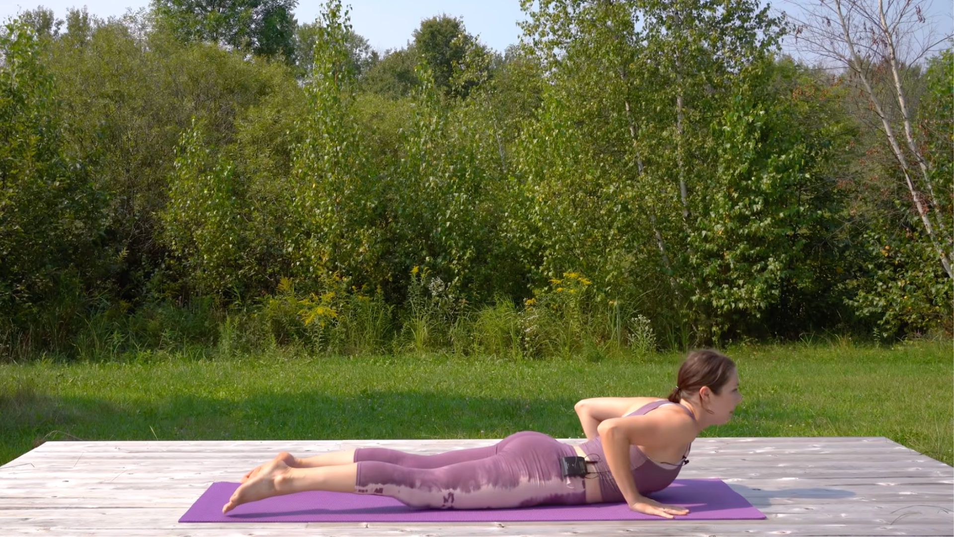 Woman lying on her belly with her hands beneath her shoulders and lifting her chest in Cobra Pose
