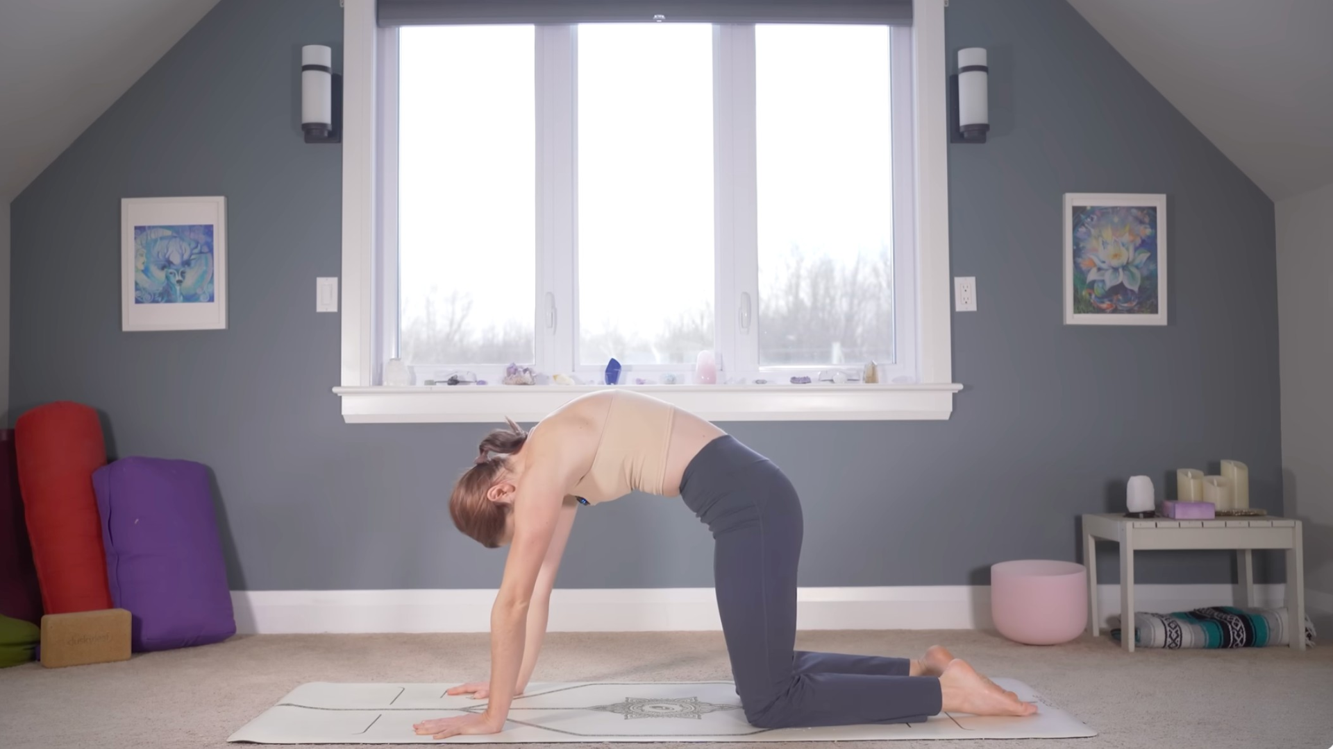 Woman kneeling on a yoga mat rounding her back in Cat Pose
