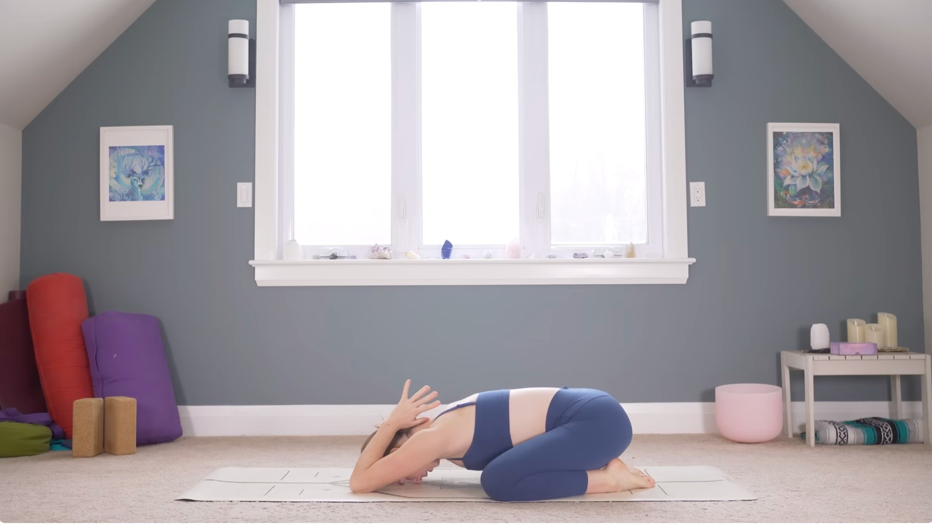 Woman kneeling on a yoga mat in Child's Pose with her thumbs near the back of her neck