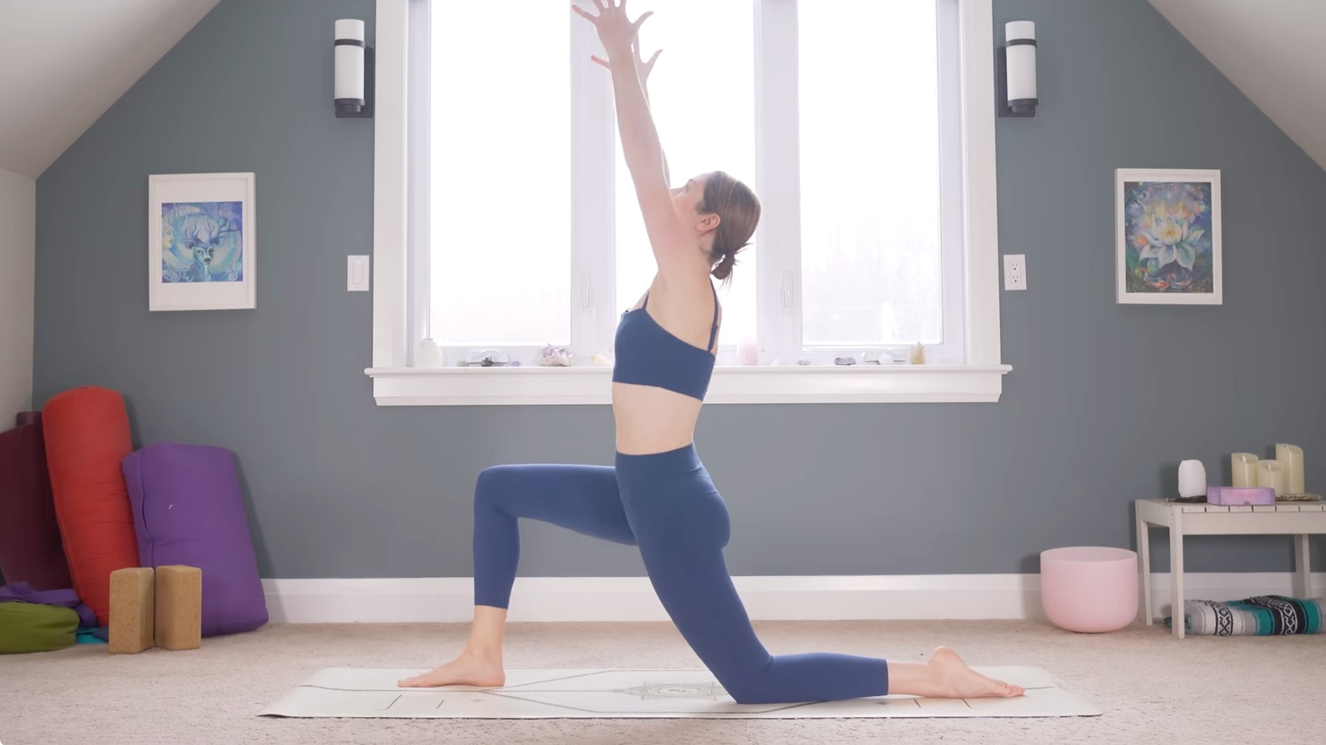 Woman kneeling in Low Lunge on a mat with her arms reaching alongside her ears