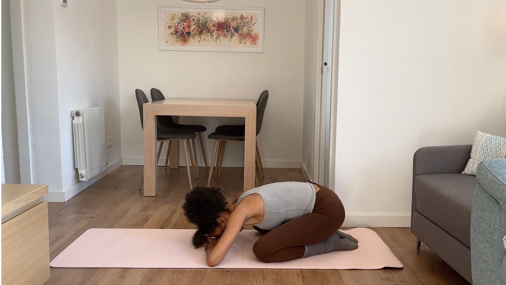 Person practicing child's pose on yoga mat in living room.