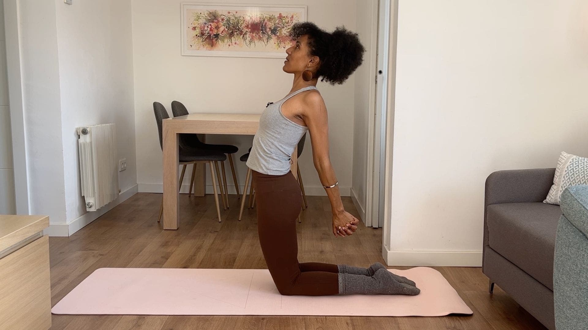 Person practicing Camel Pose on yoga mat in living room.