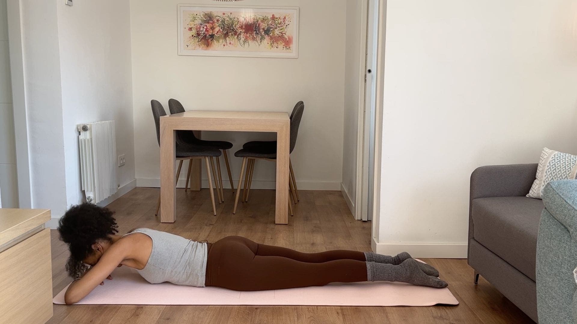 Person practicing crocodile pose on yoga mat in living room.
