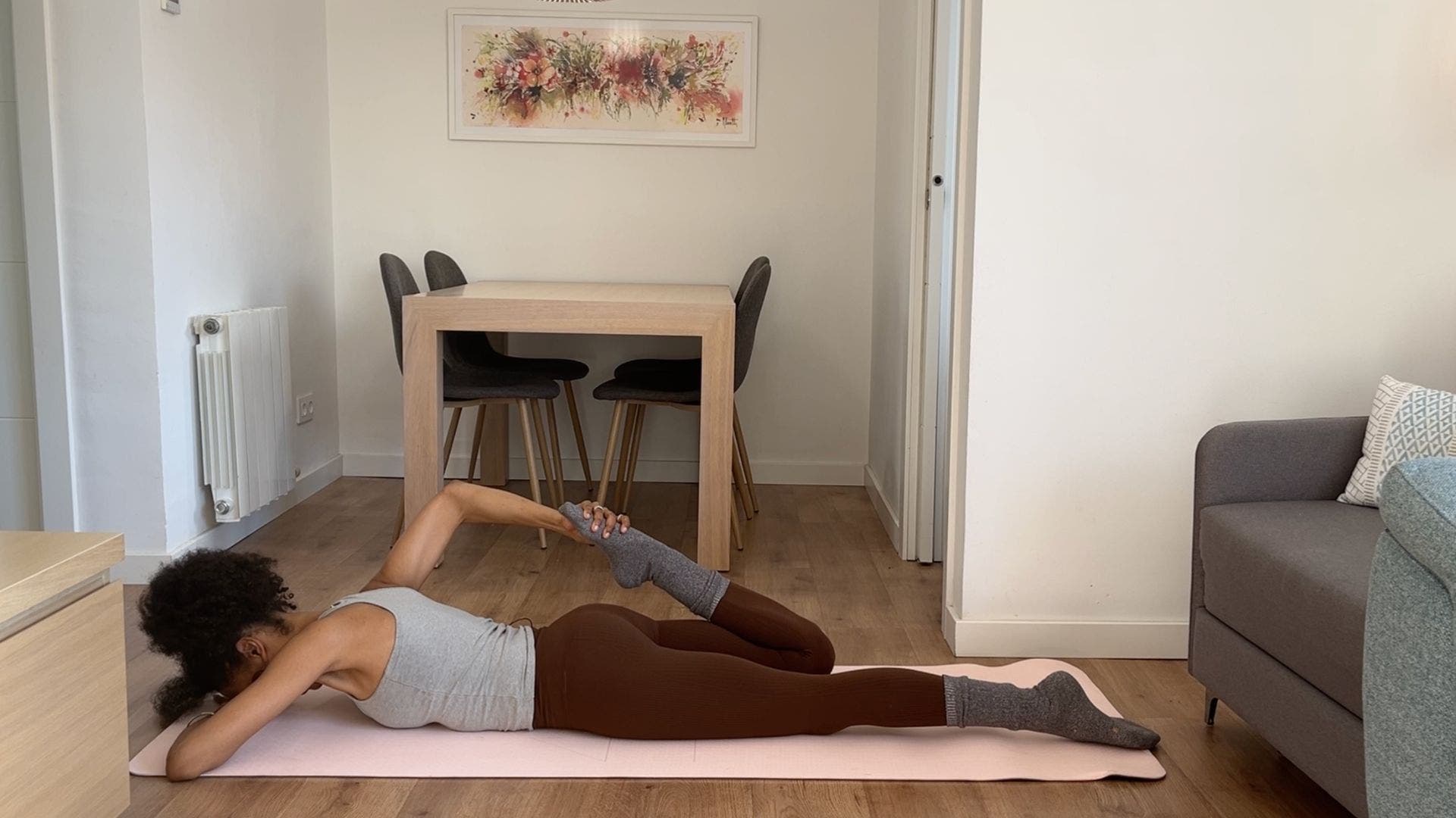 Person practicing one-legged bow pose stretch on yoga mat in living room.