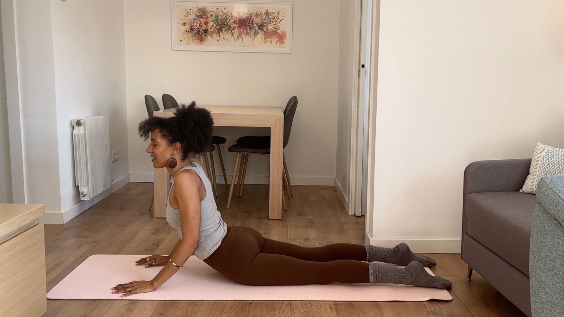 Person practicing Cobra Pose on yoga mat in living room.