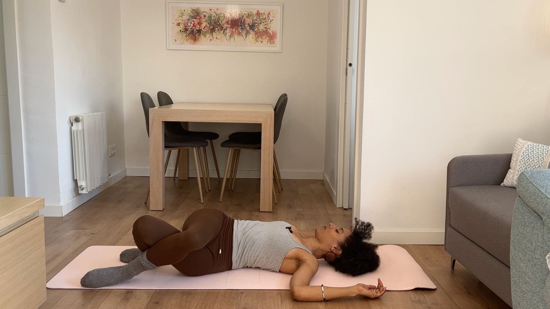 Person practicing Supine Spinal Twist on yoga mat in living room.