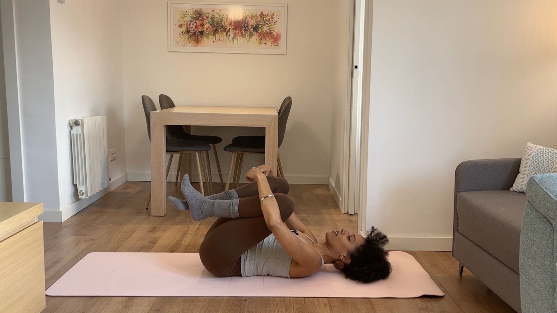 Person practicing Wind Relieving Pose on yoga mat in living room.