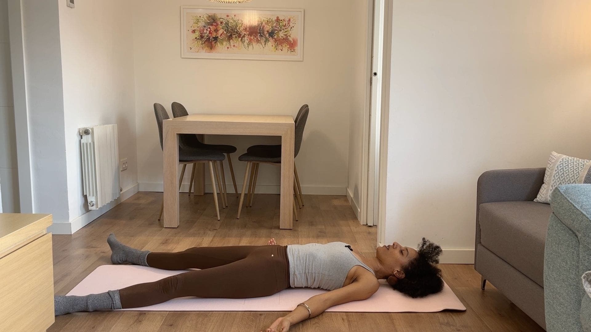 Person practicing Savasana on yoga mat in living room.