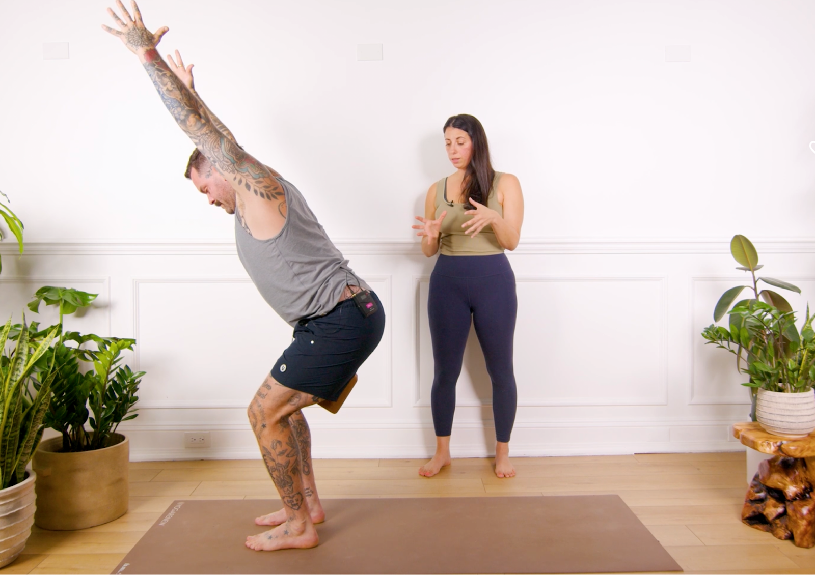 Man practicing chair pose on yoga mat while woman instructs.