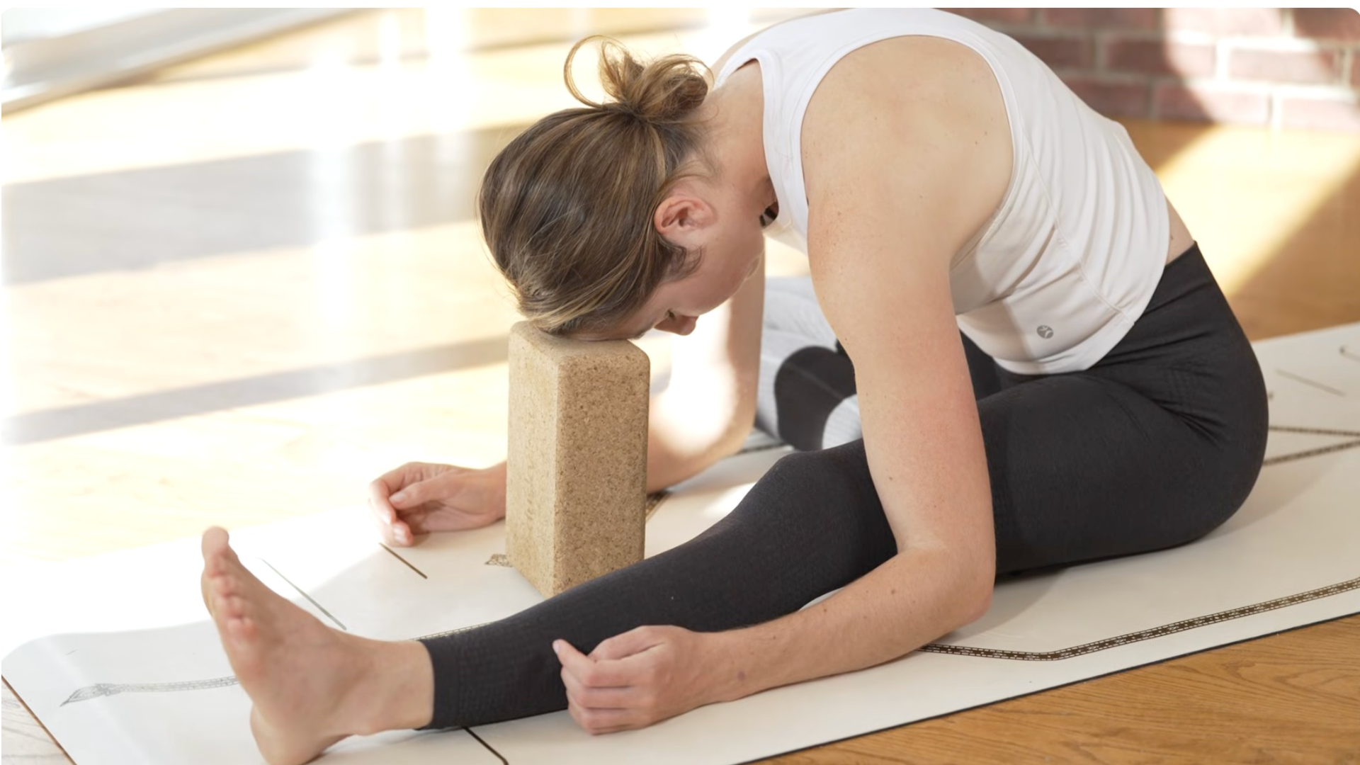 Woman sitting in a forward bend during a yin yoga sequence with one leg straight and the other knee bent