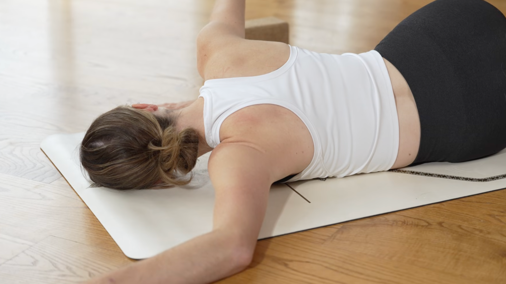 Close-up shot of the upper body of a yoga teacher practicing Broken Wing as a stretch for her left shoulder