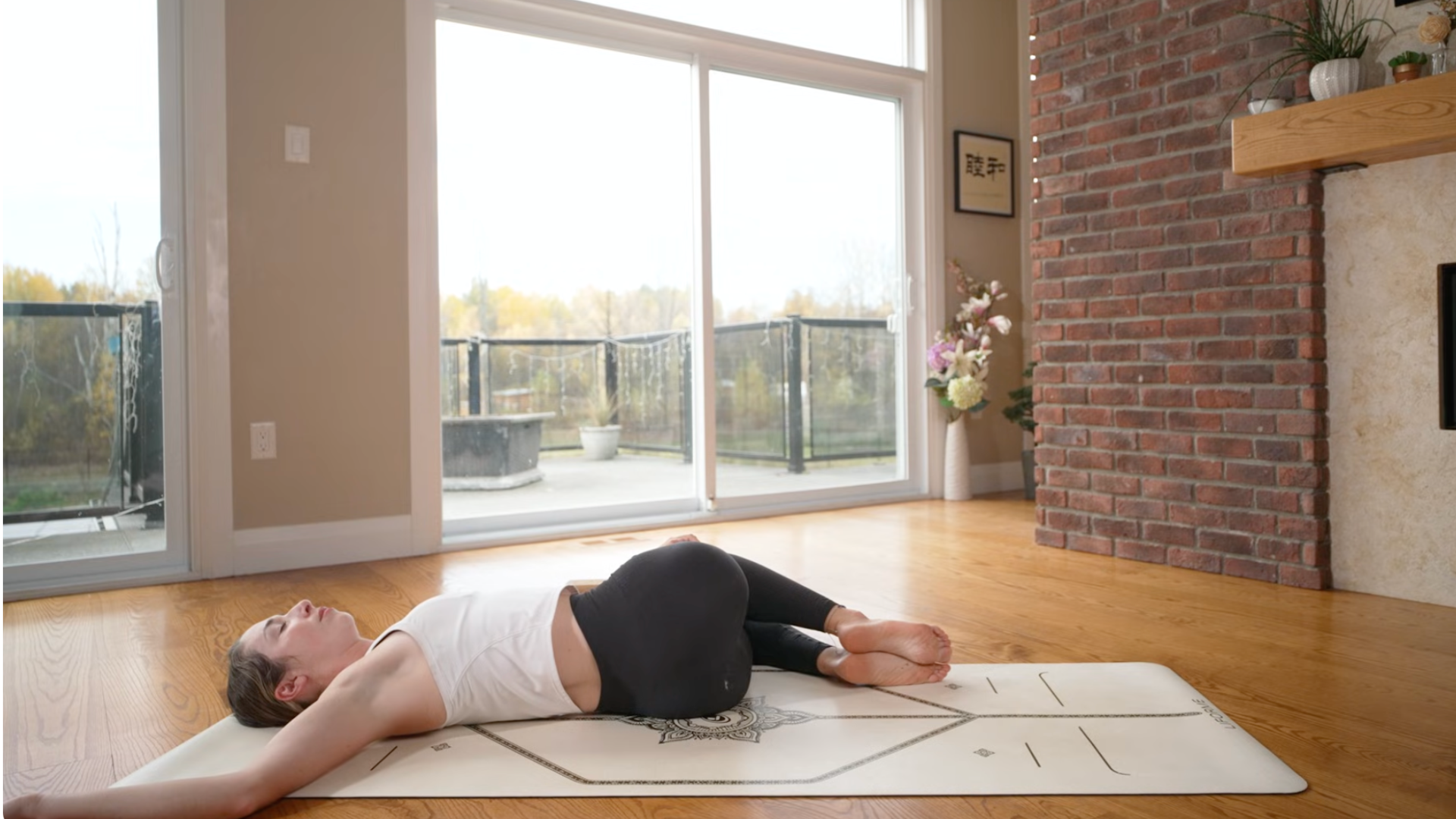Woman reclining on a yoga mat practicing a reclined twist with both knees bent and leaning toward the left