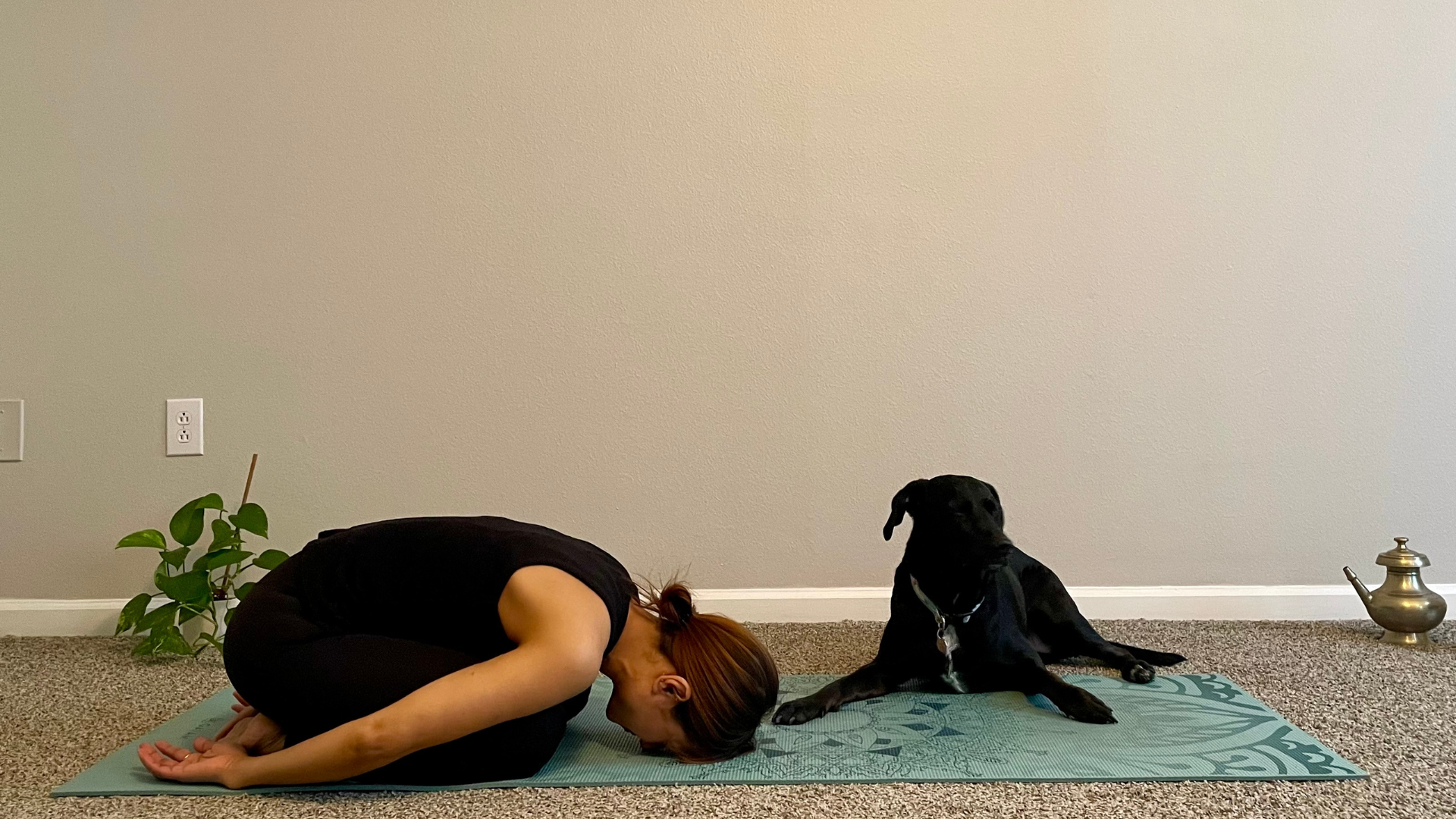Woman on a yoga mat in Child's Pose with her arms outstretched alongside her body
