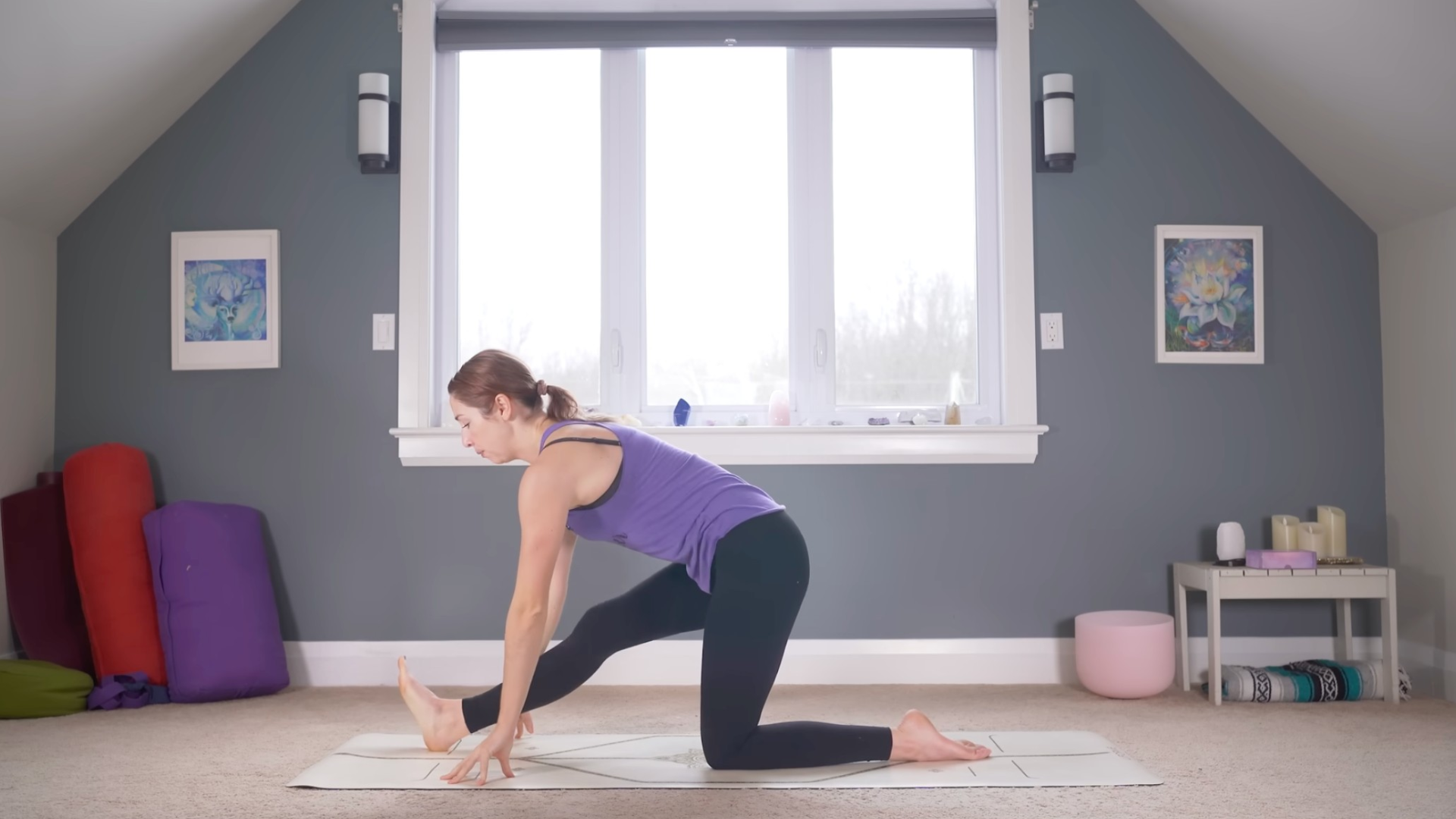 Woman kneeling on a mat with her right leg straight as she leans forward with her fingertips on the mat