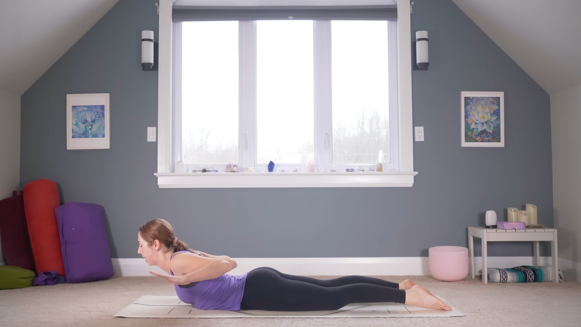 Woman lying on her belly on a mat while lifting her chest and hands off the mat