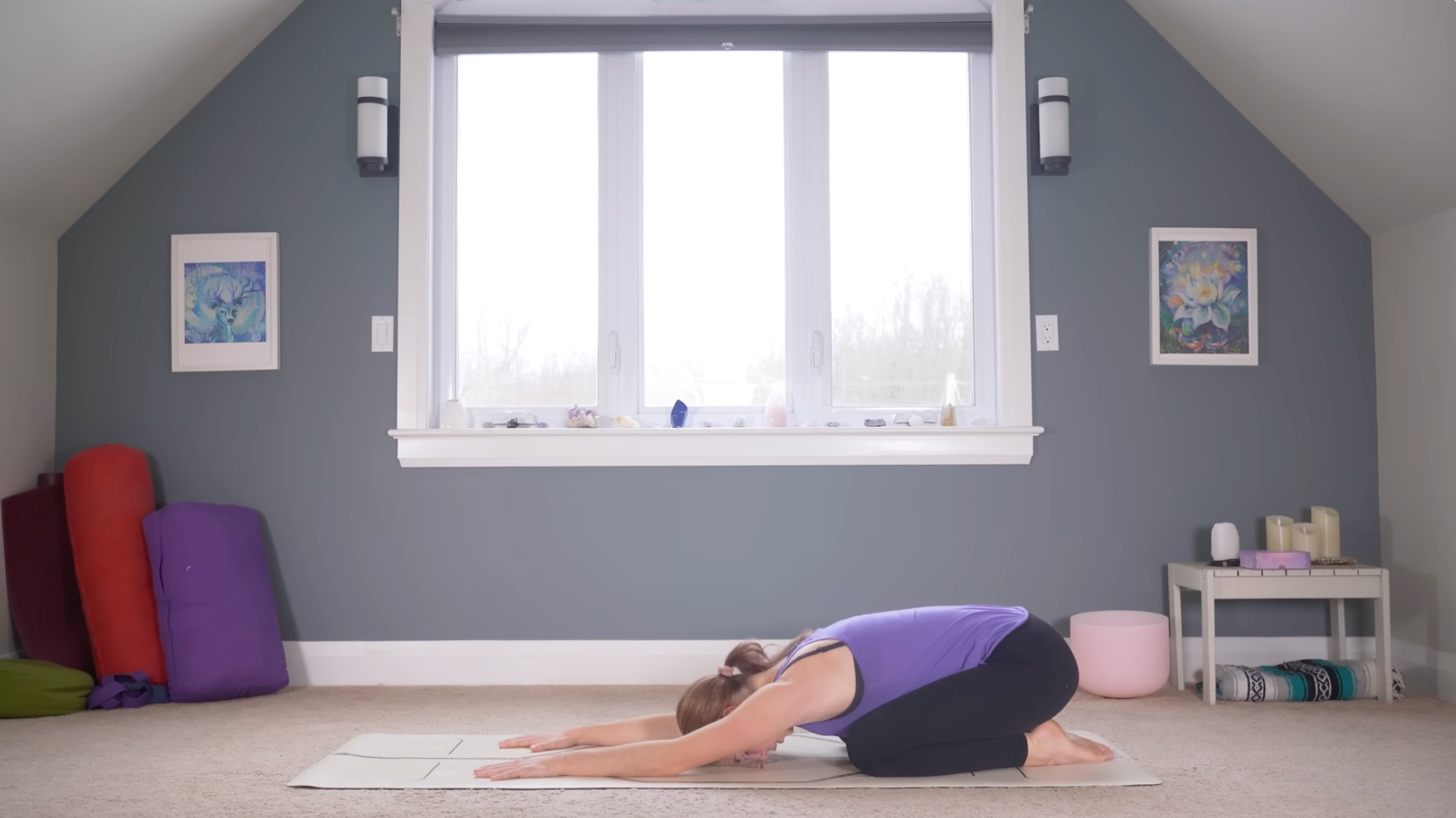 Woman resting her forehead and knees on a mat while extending her arms alongside her ears