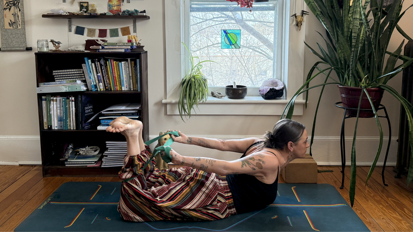 Woman lying on her stomach on a mat, reaching towards her ankles