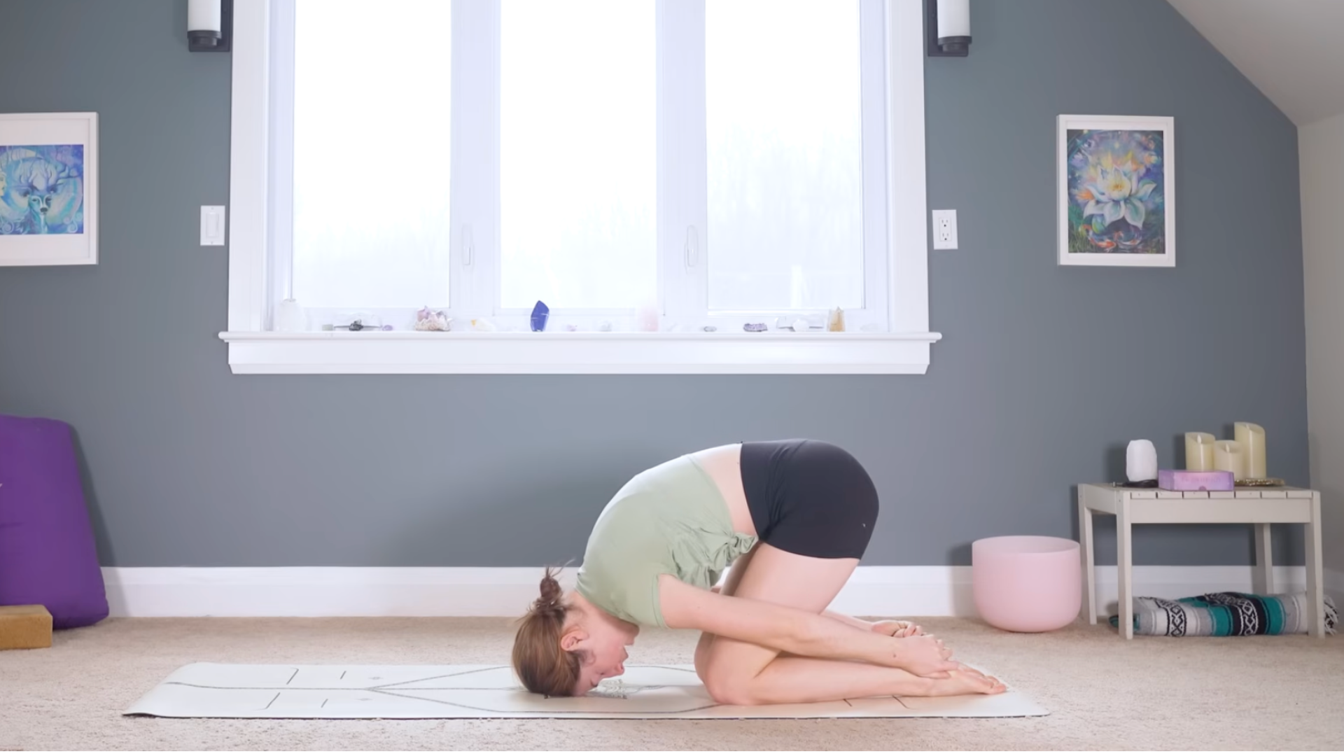 Woman kneeling on a mat and leaning forward with her forehead on the mat and her hands reaching behind her for her heels