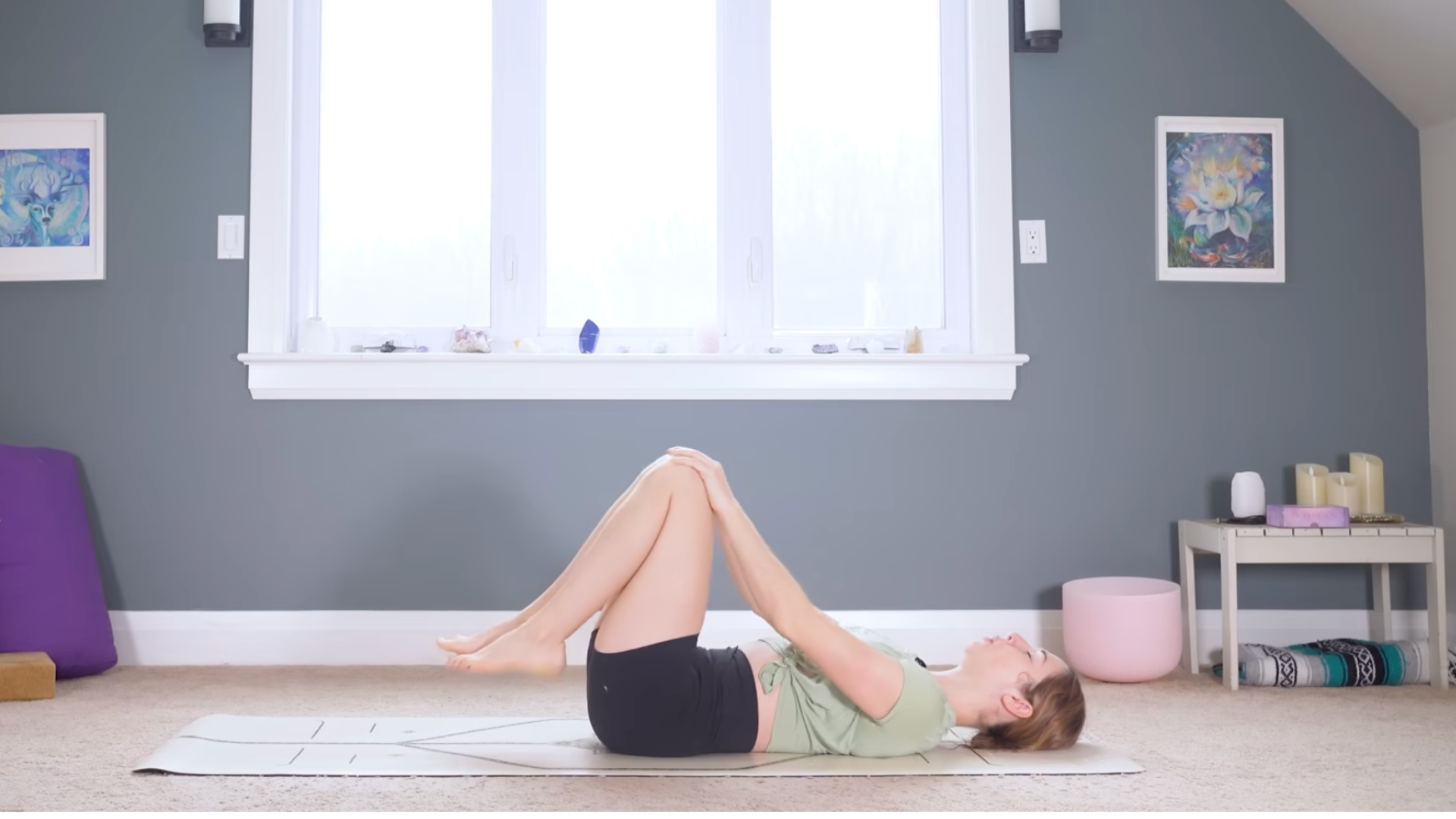 Woman lying on her back on a mat drawing her knees toward her chest during a 10-minute morning yoga for back tightness class