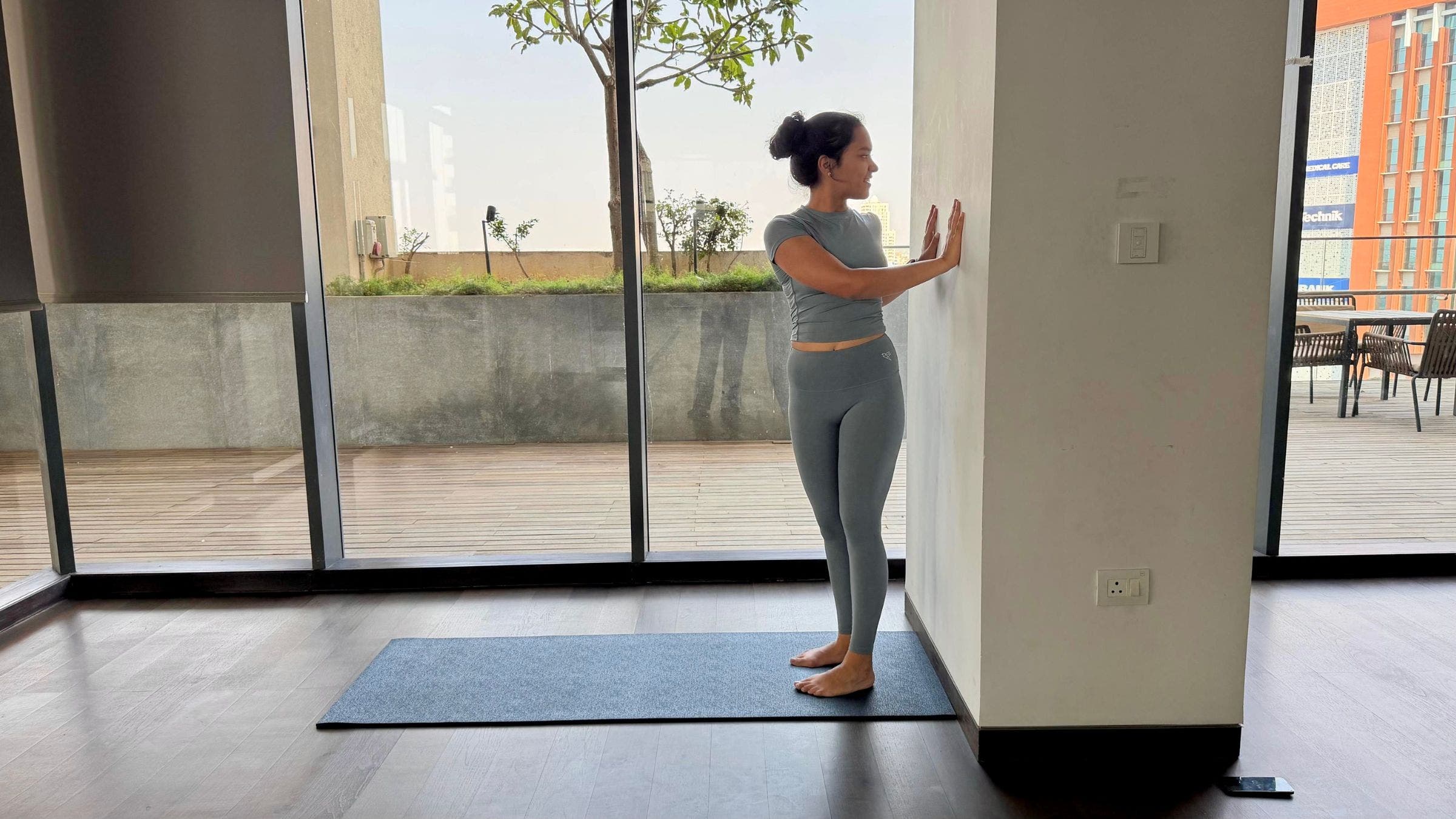 Riya Davda practicing standing twist against a wall.