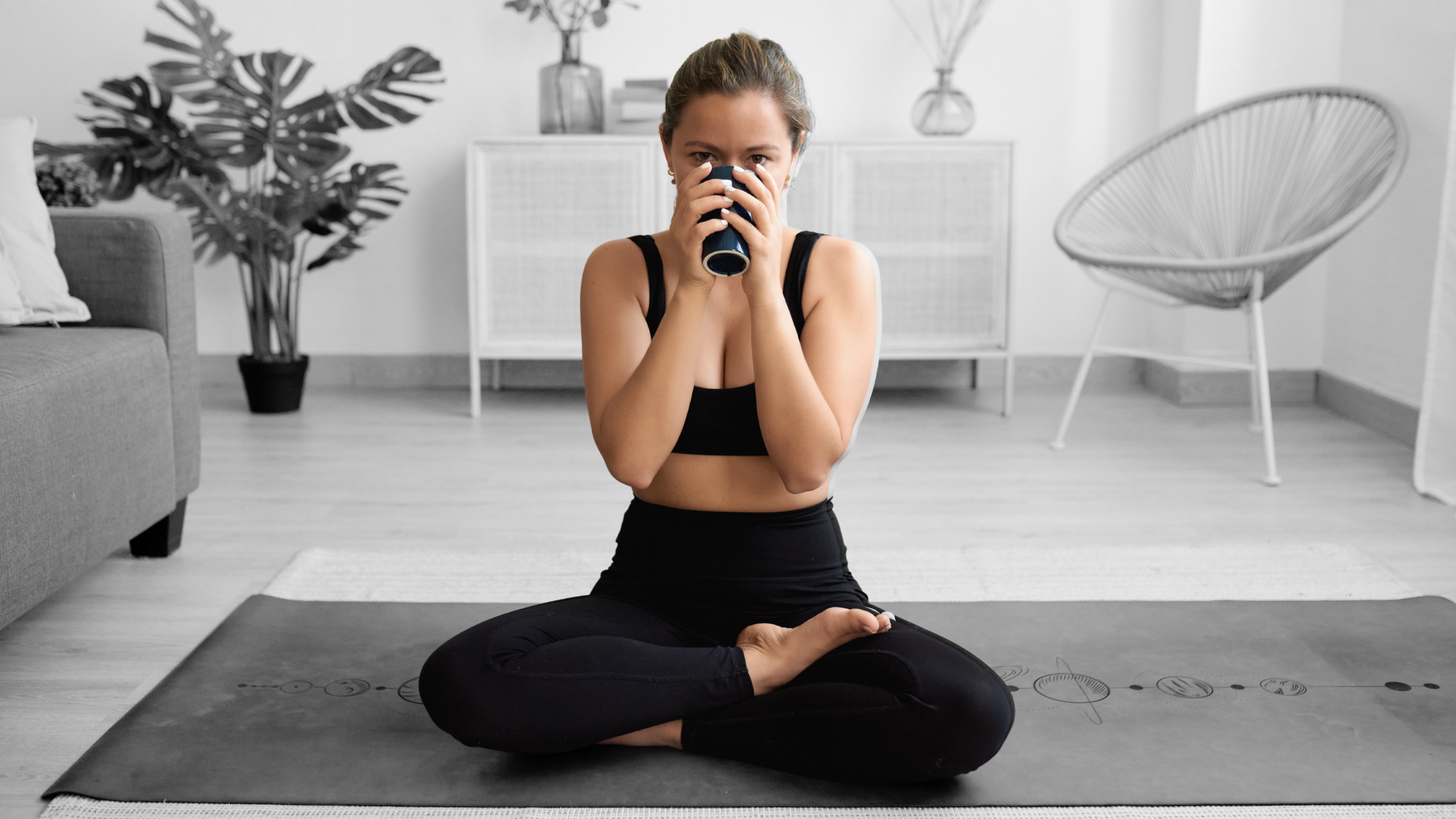 A woman drinking coffee while sitting on a yoga mat