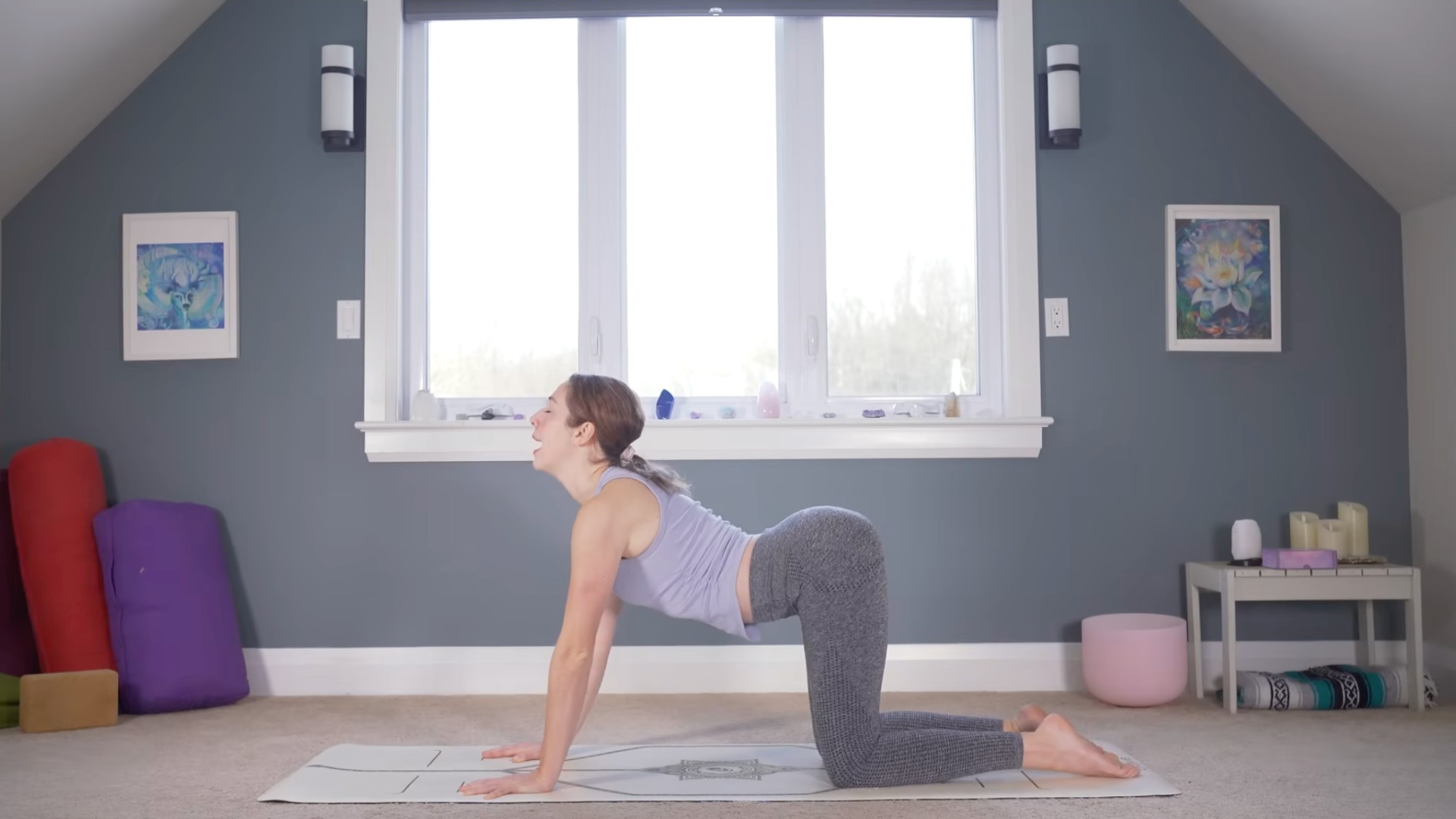 Woman kneeling on a mat practicing Cow Pose in yoga by taking a slight backbend
