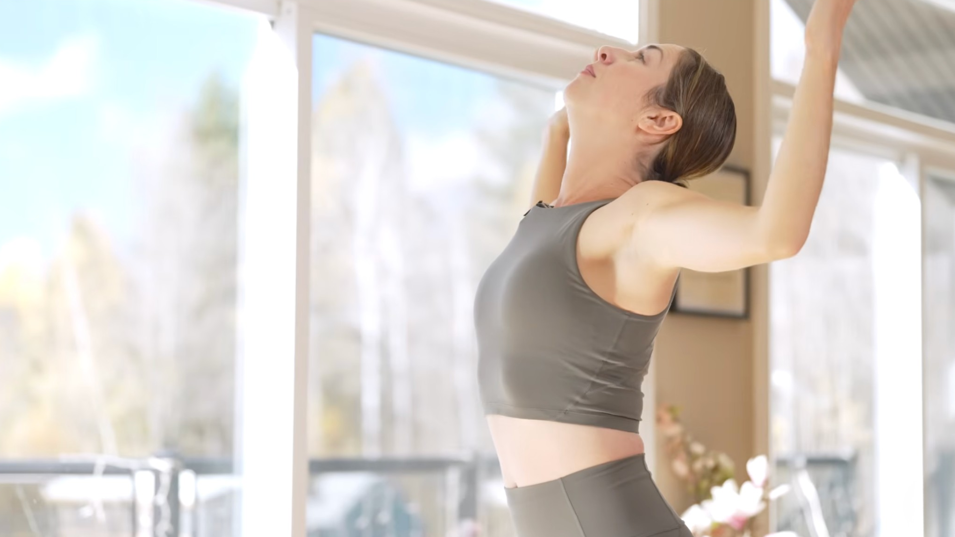 Woman standing in a slight backbend with her arms at 90 degrees as she lifts her chest