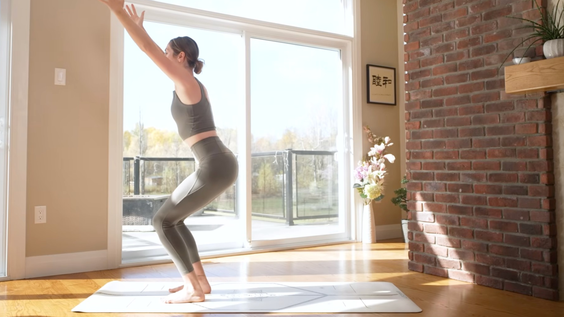 Woman doing standing yoga while bending her knees and reaching her arms alongside her head in a standing yoga practice