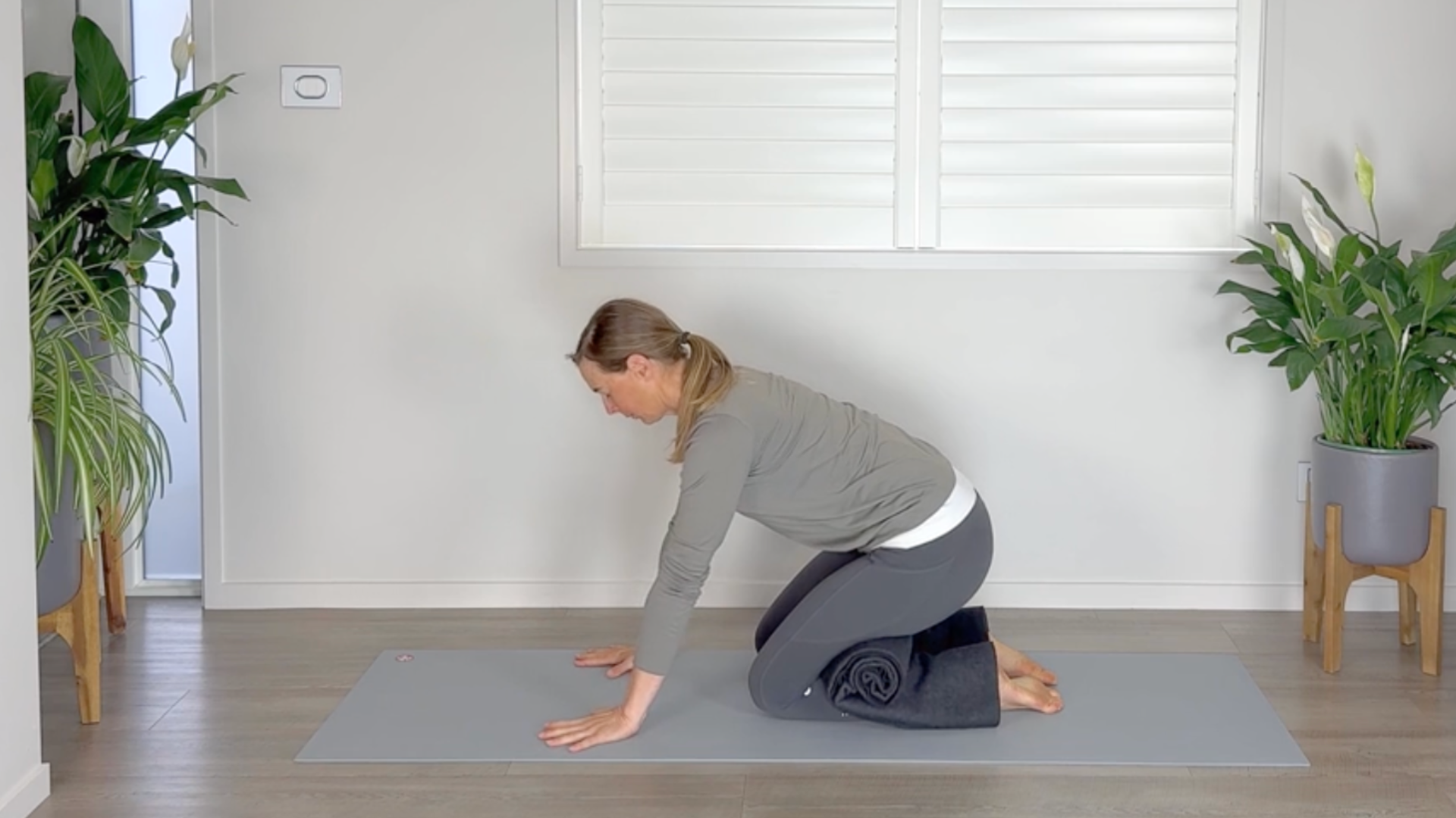 Woman kneels with her hips dipping toward her heels with a blanket draped over her legs