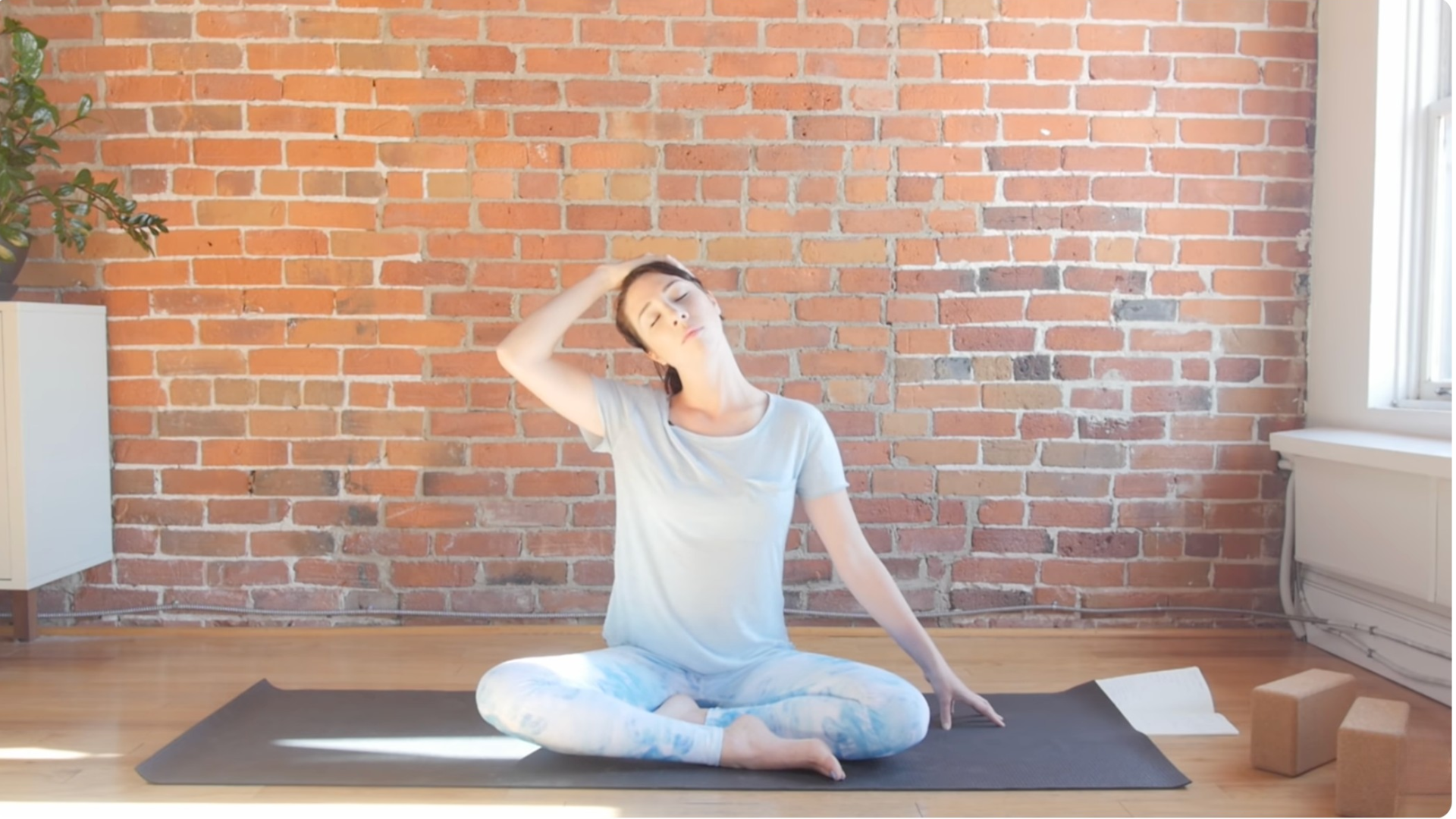 Woman sitting on a mat while leaning her head toward one shoulder